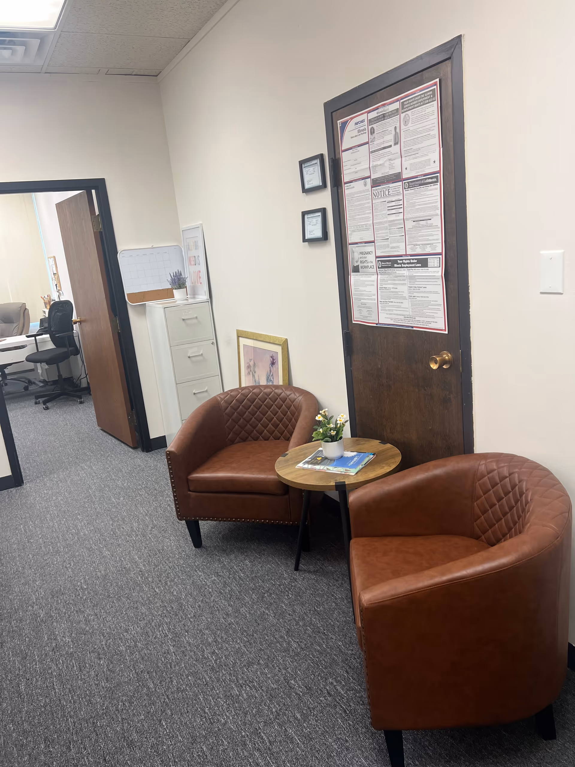 Two brown quilted leather chairs surround a small round table in a waiting area.