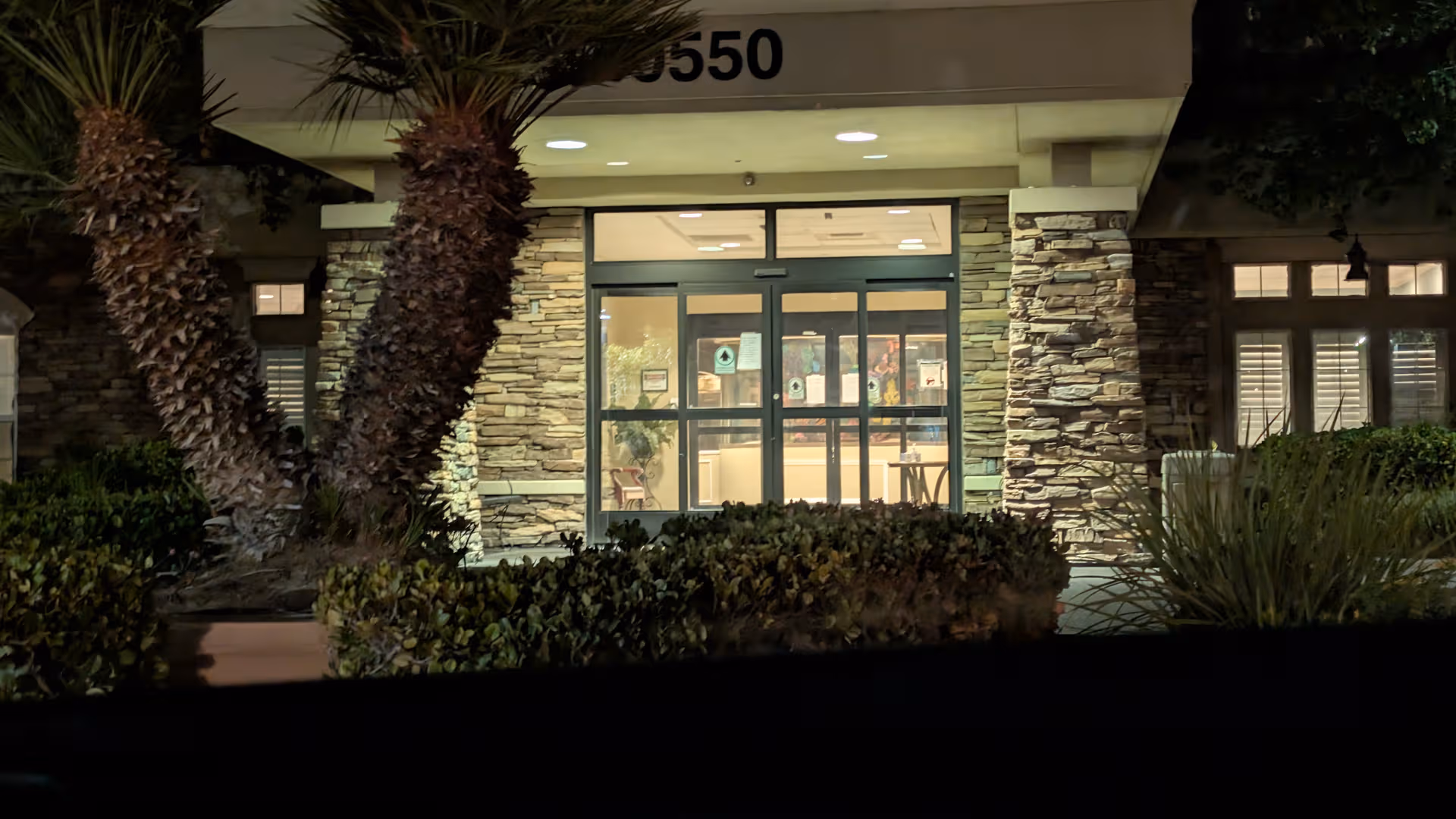 Nighttime view of a stone-faced senior living facility entrance with glass doors.