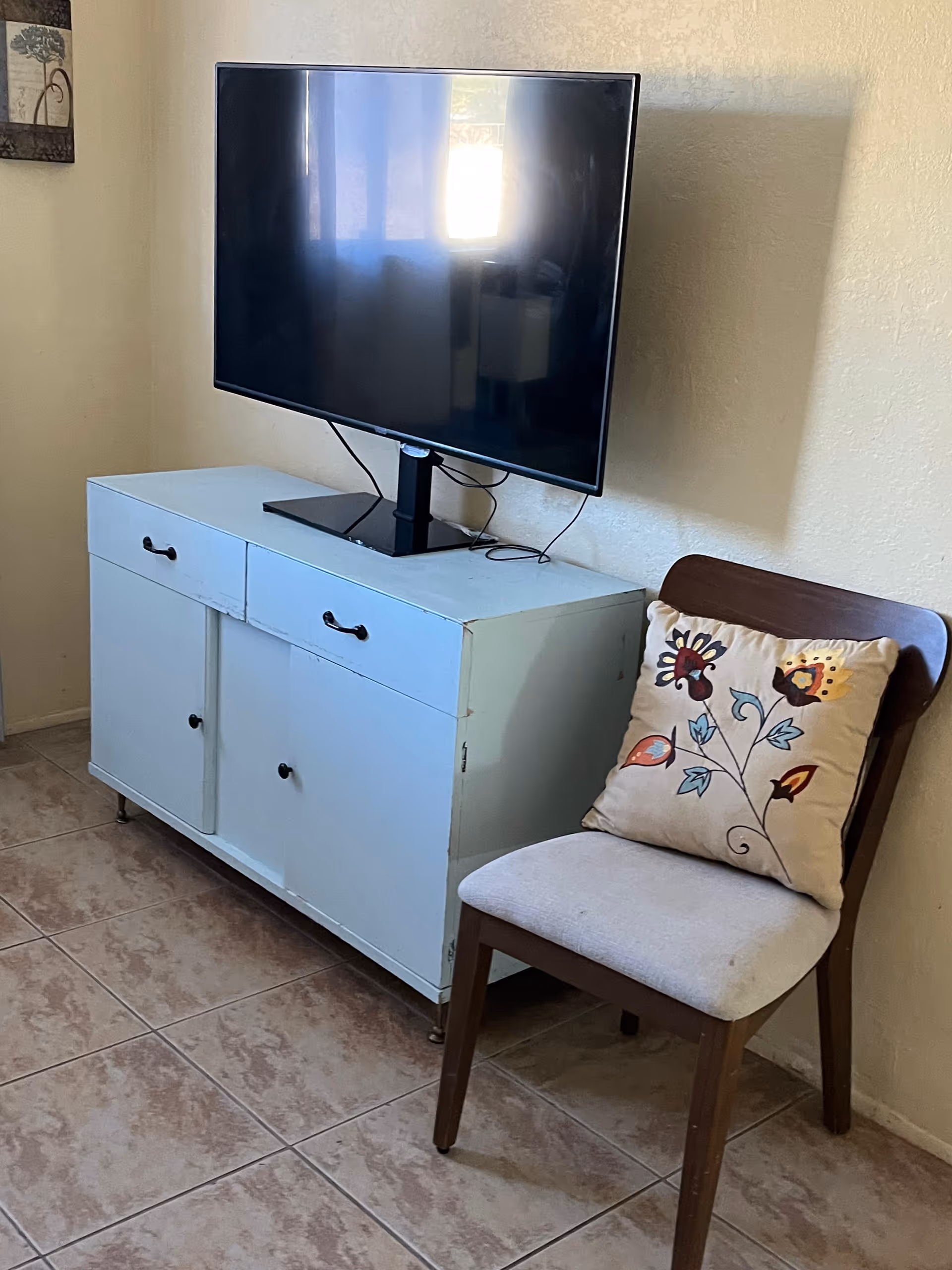 Flat screen TV sits on a light blue cabinet beside a cushioned wooden chair.