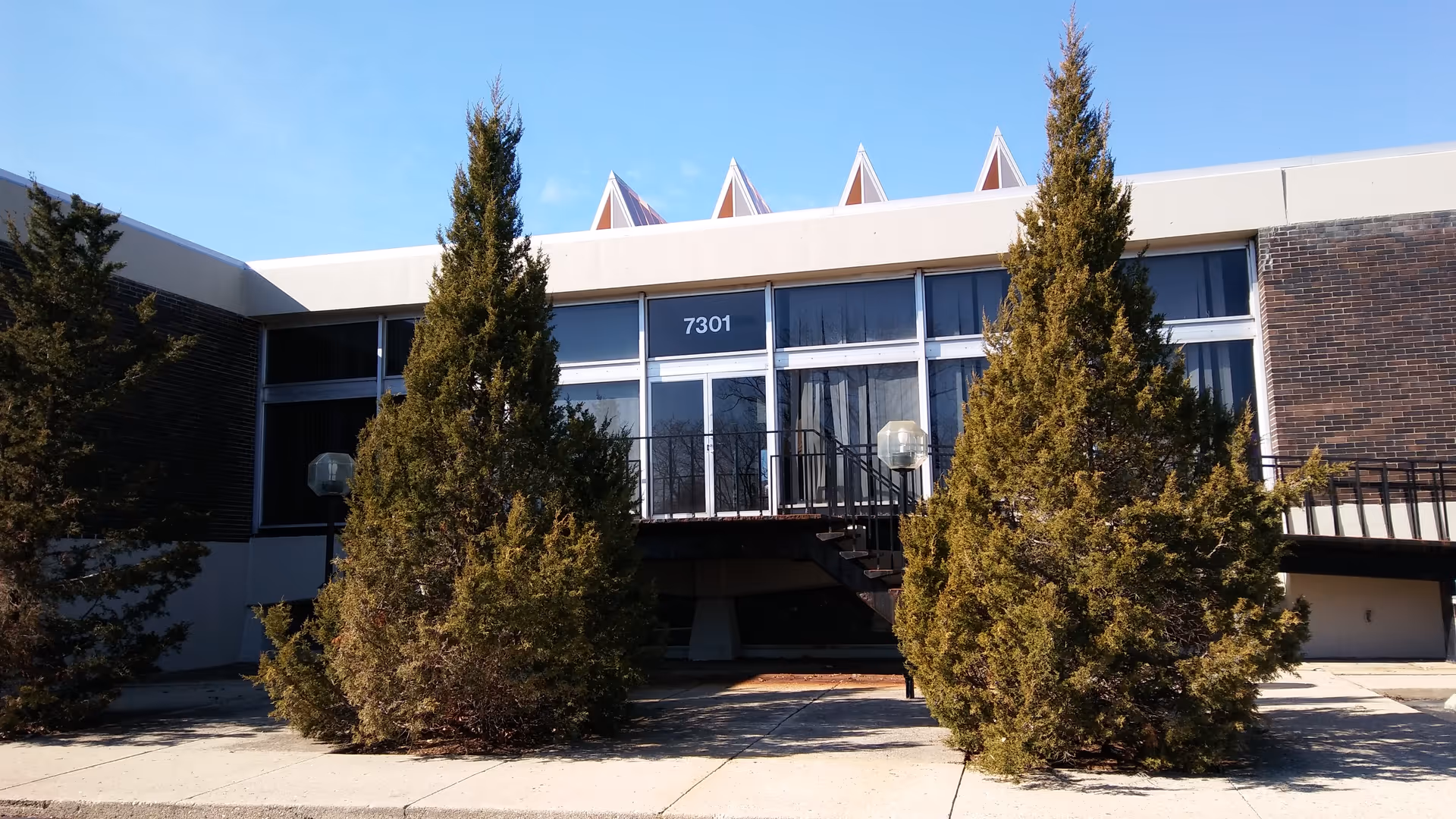Front exterior of a DMAZ Corporation senior living facility with tall conifer trees.