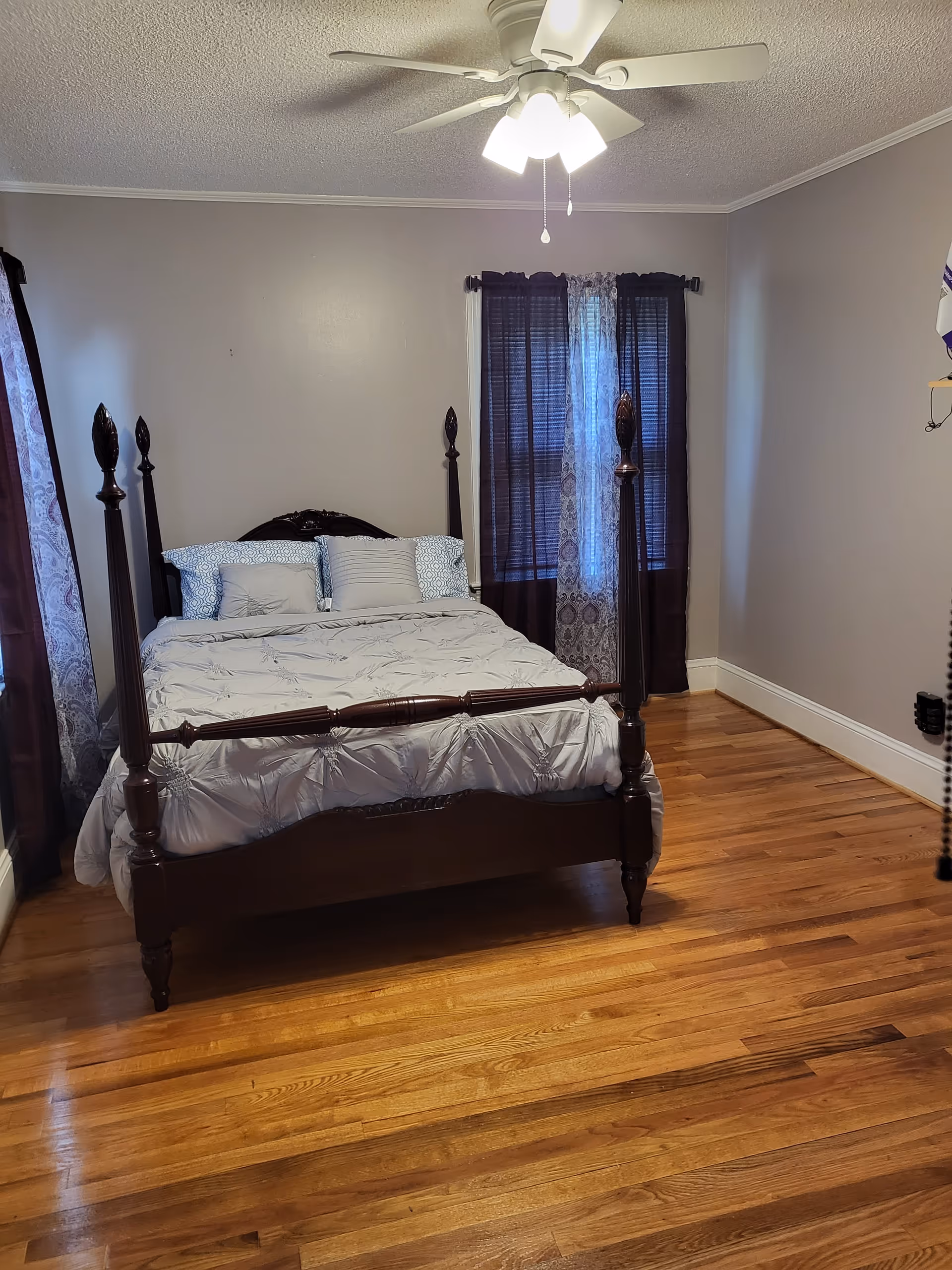 A dark wooden four-poster bed sits in a gray bedroom with hardwood floors.