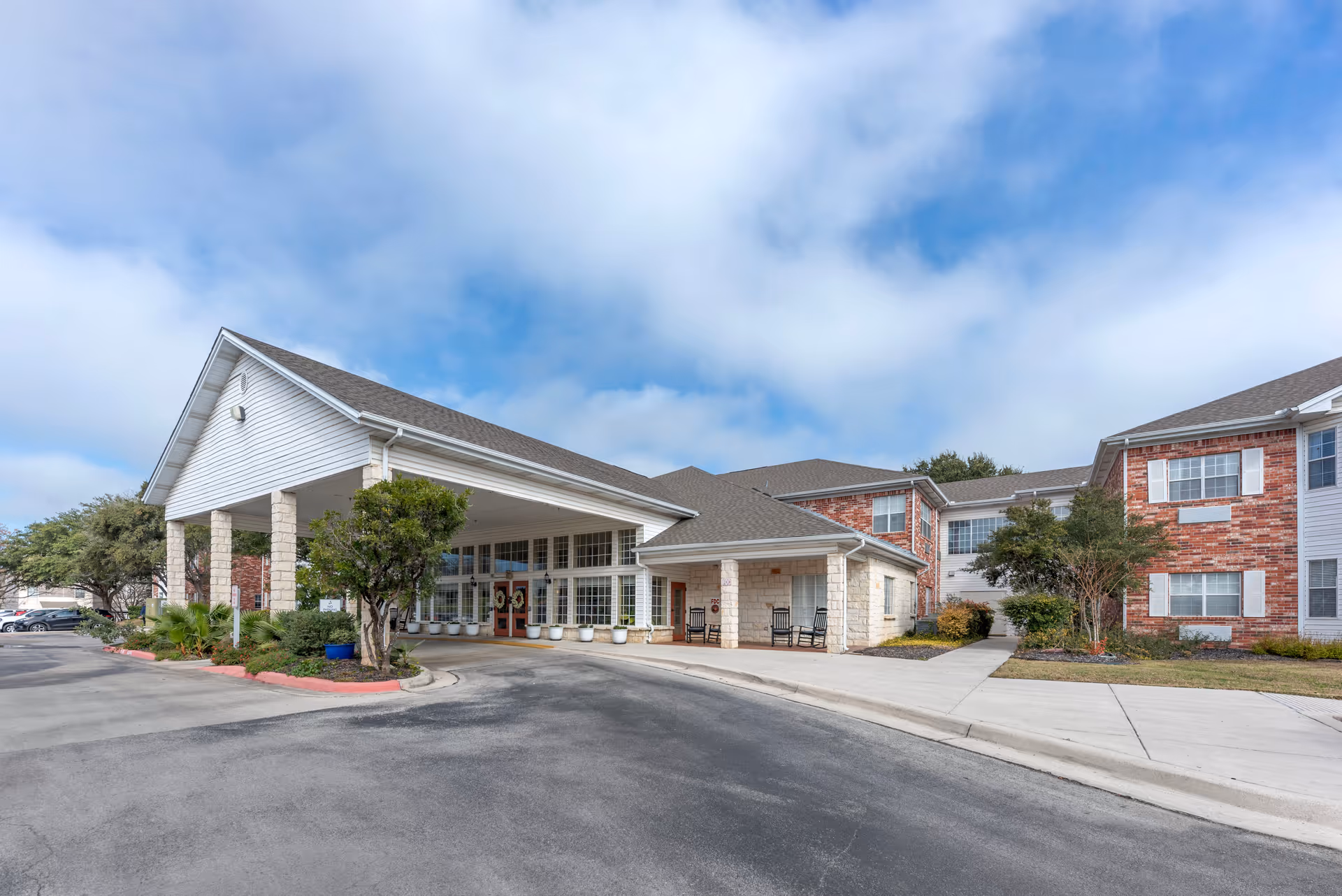 Front entrance of a brick-and-siding senior living facility with a covered porte-cochere and driveway.