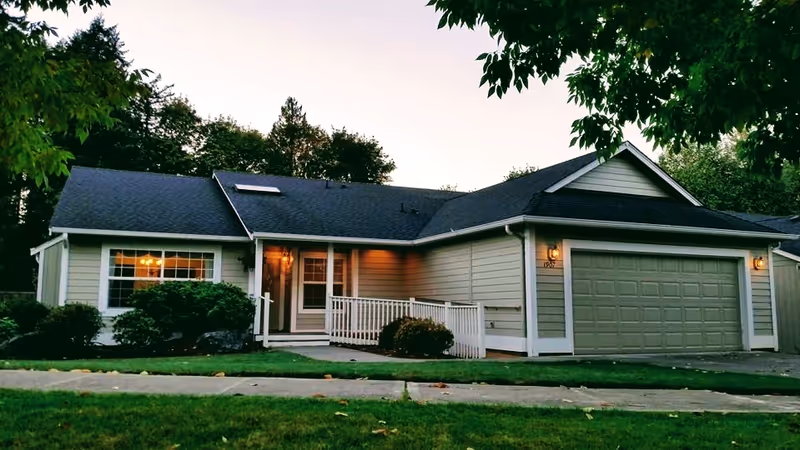 Single-story, suburban-style house with a front porch and two-car garage at dusk.