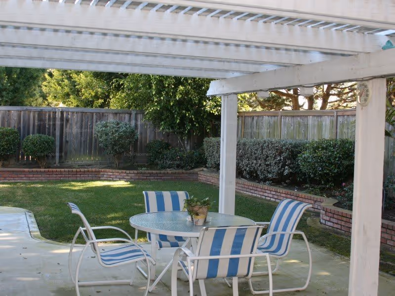 Outdoor patio with blue and white striped chairs around a glass table under a white pergola.