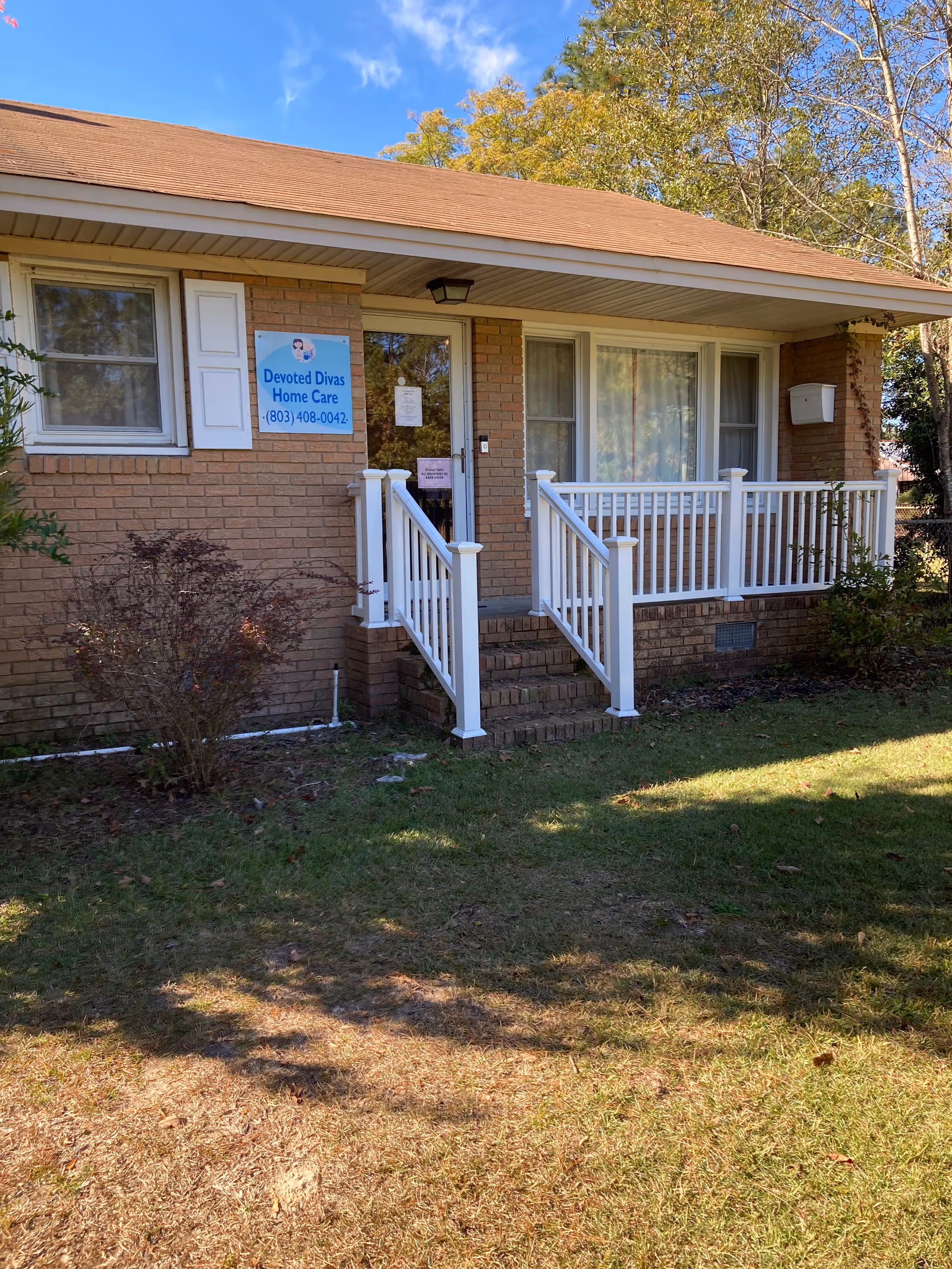 Brick building front with white railing, steps, and a sign for Devoted Divas Home Care.