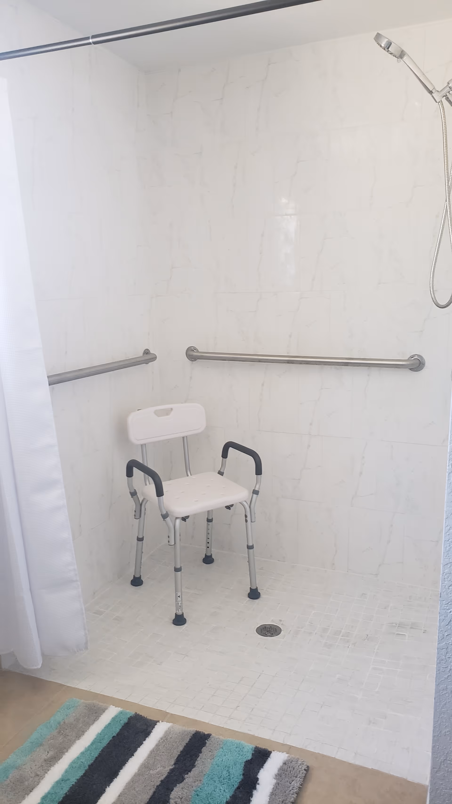 Wheelchair-accessible shower with a chair and grab bars in a tiled bathroom.