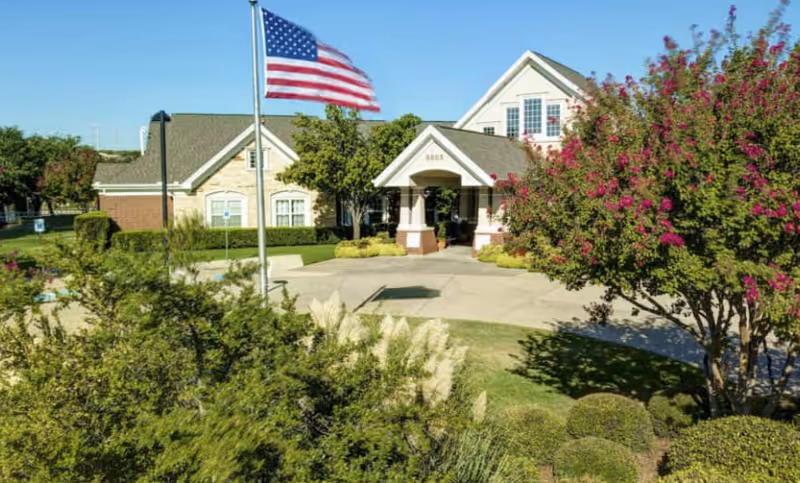 The Auberge at Valley Ranch exterior with flag, entrance, and landscaped front yard.