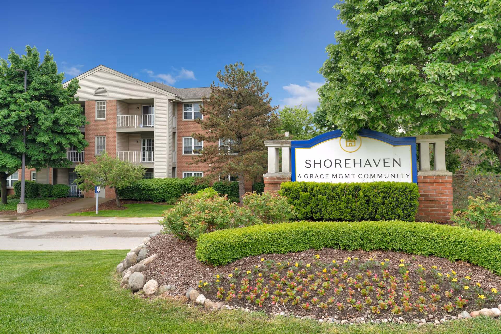 Exterior view of Shorehaven senior living facility with brick building, landscaped sign, and greenery.