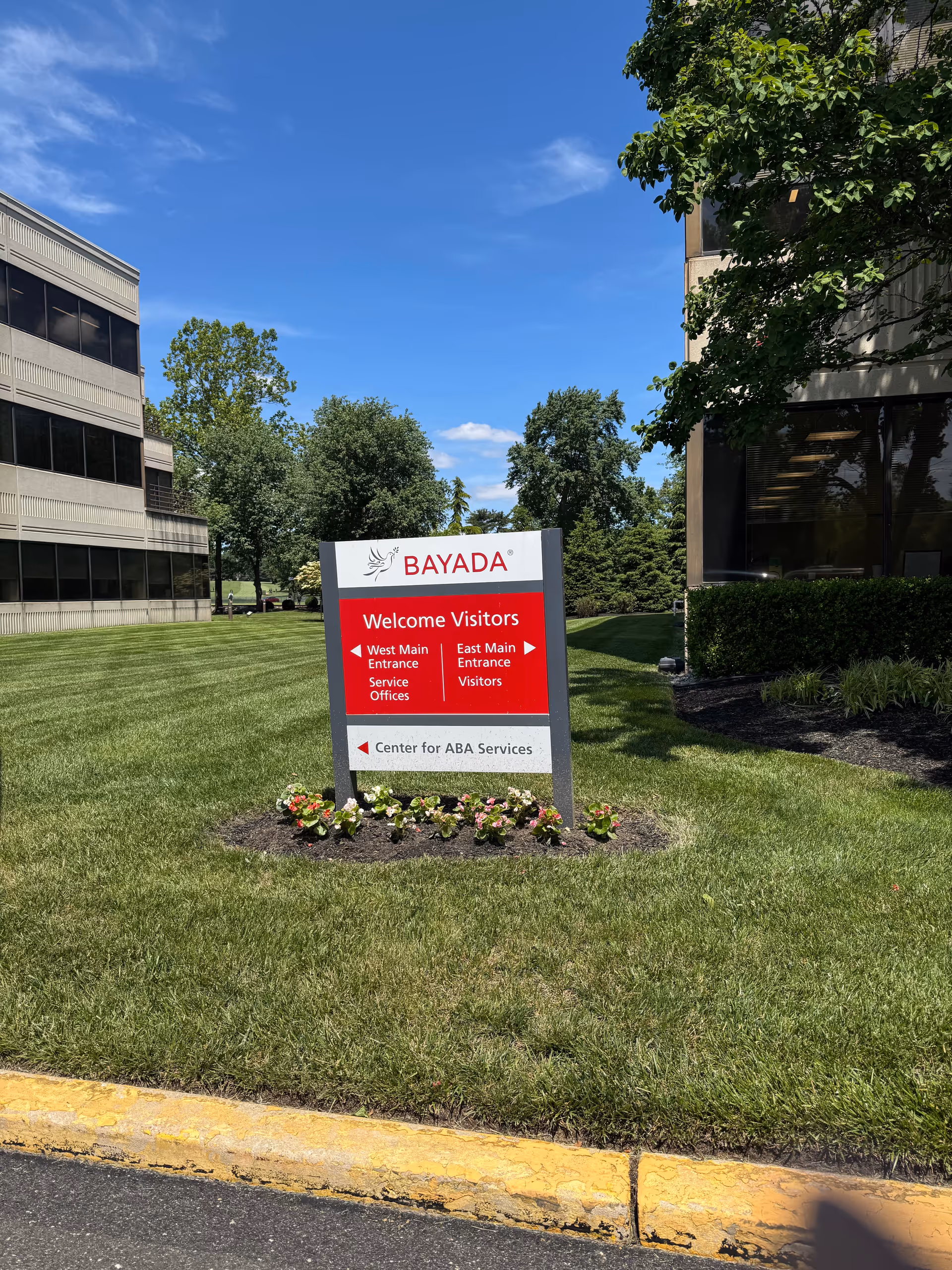 A BAYADA welcome sign sits on a grassy lawn near office buildings.
