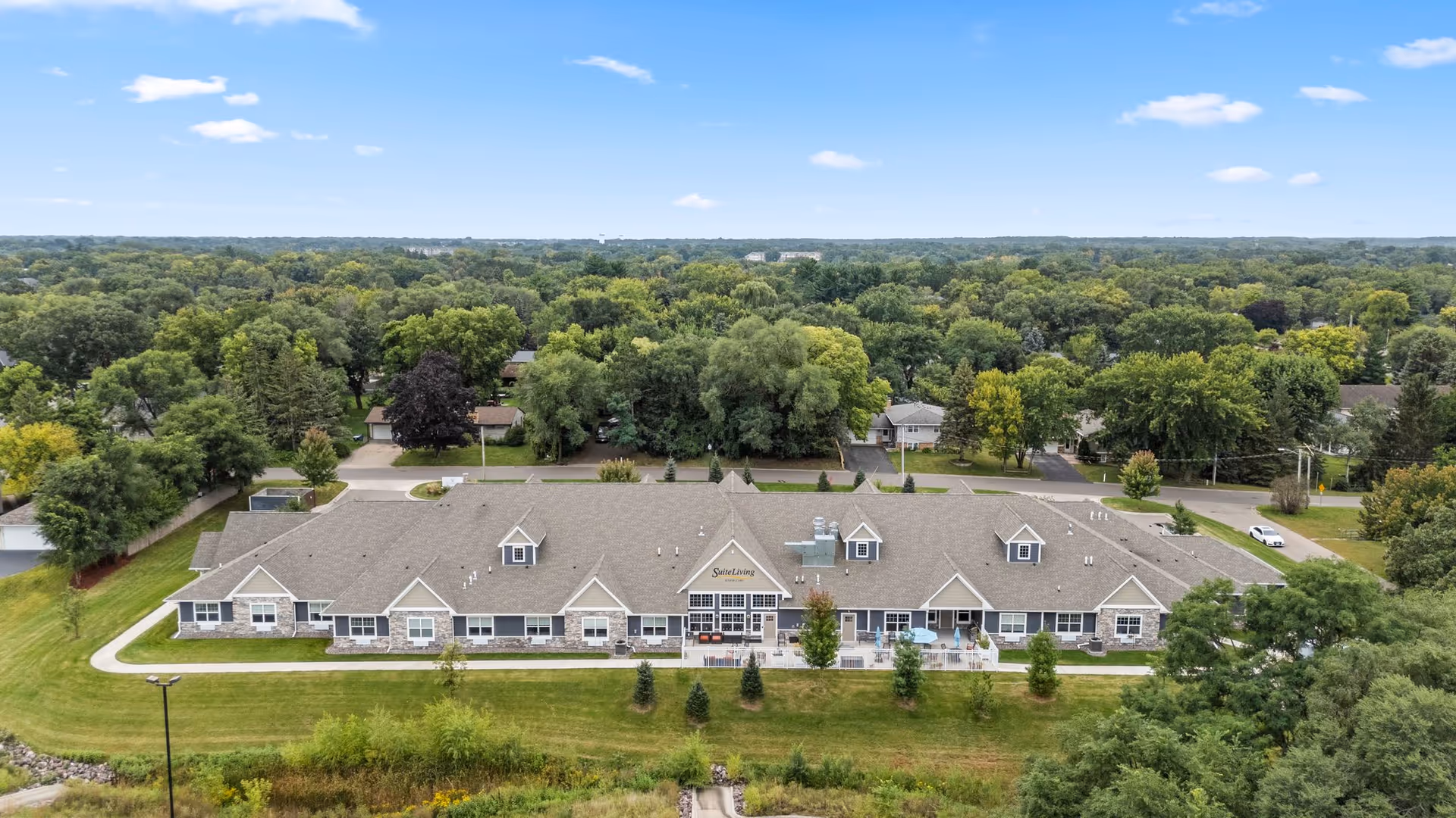 Aerial view of a single-story senior living building with a central entrance and surrounding trees.