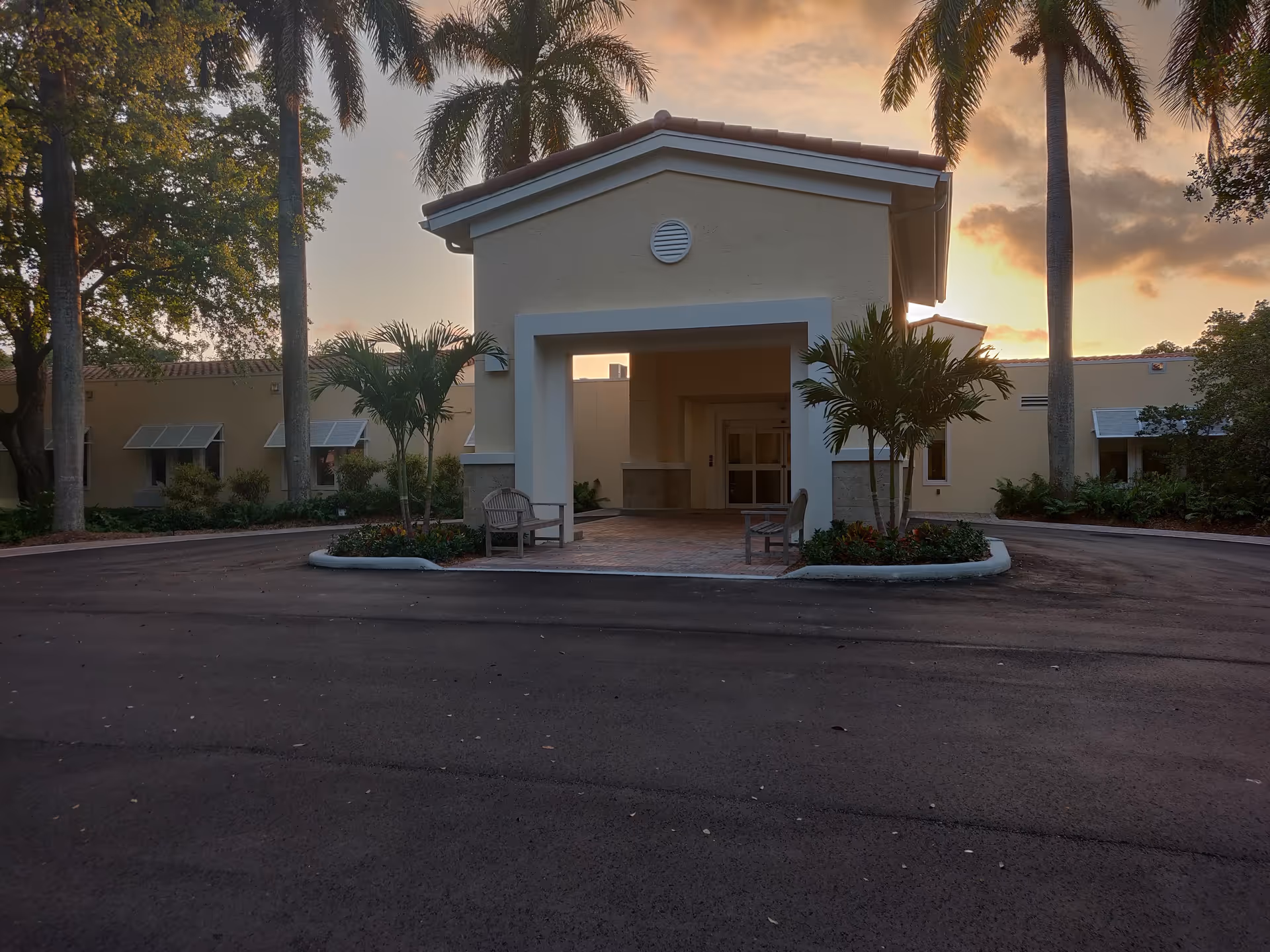 Sunset-lit entrance of Hospice by the Sea exterior with benches and palms.