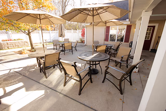 Outdoor patio with round tables, chairs, and umbrellas on a concrete courtyard next to a building.