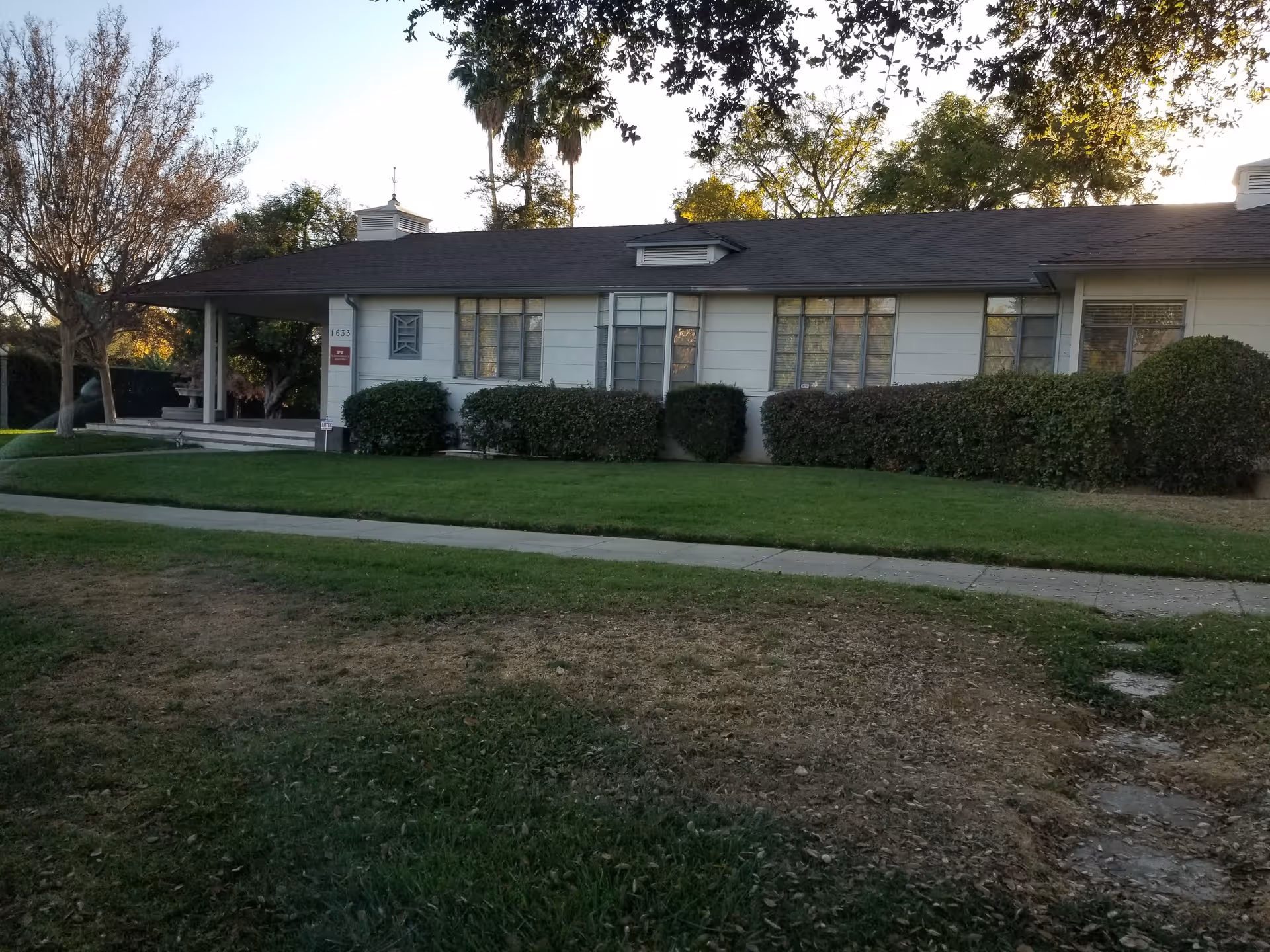 Single-story facility exterior with manicured hedges, lawn, and a sidewalk along the front.