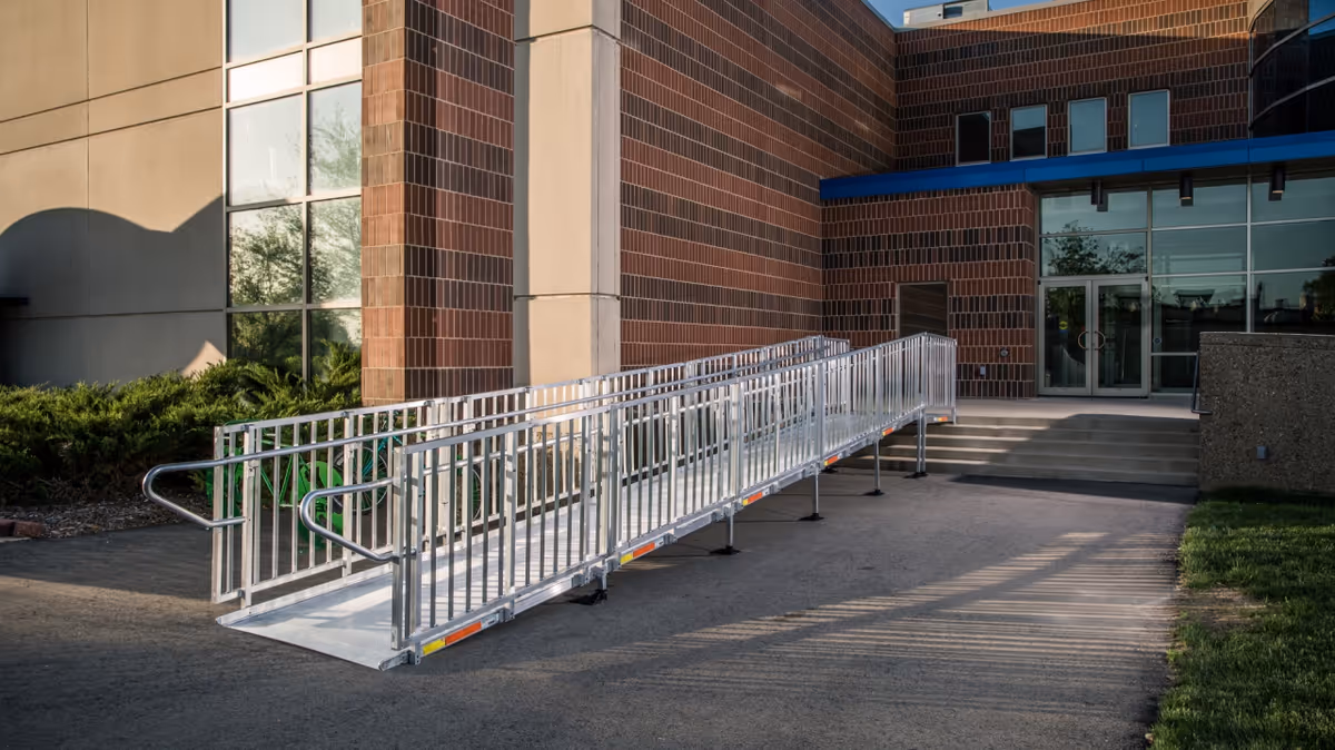 Exterior view of a brick senior living facility with a long metal ramp to the entrance.