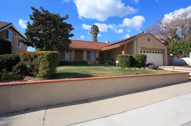 Exterior view of a single-story tan house with a red-tiled roof and front yard.