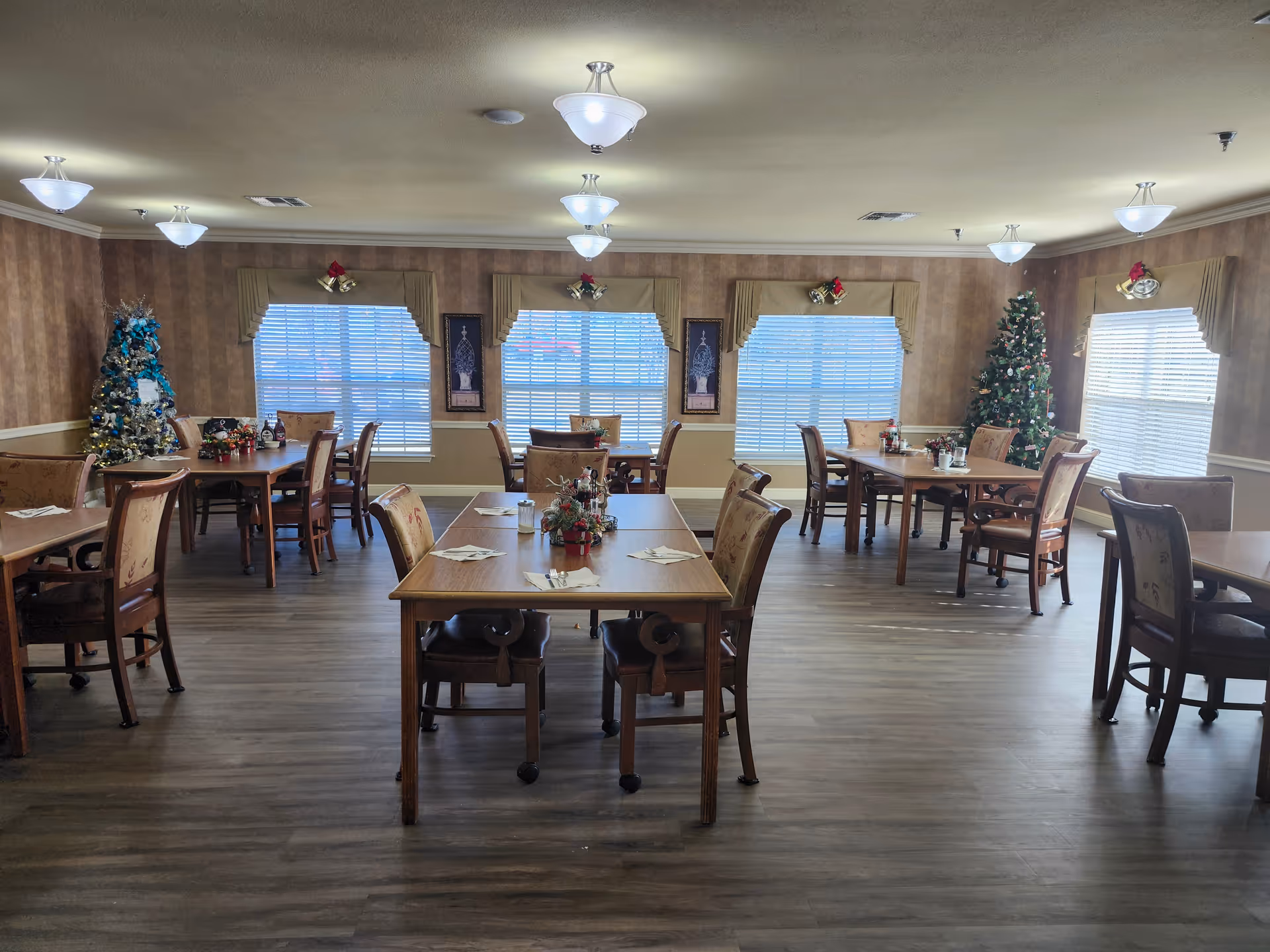 Seasonal decor and Christmas trees decorate a large senior living dining hall.