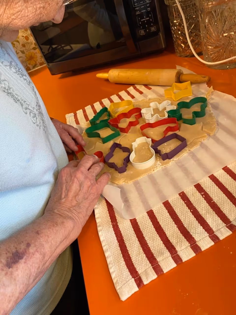 An elderly person cuts dough with cookie cutters on a kitchen counter.