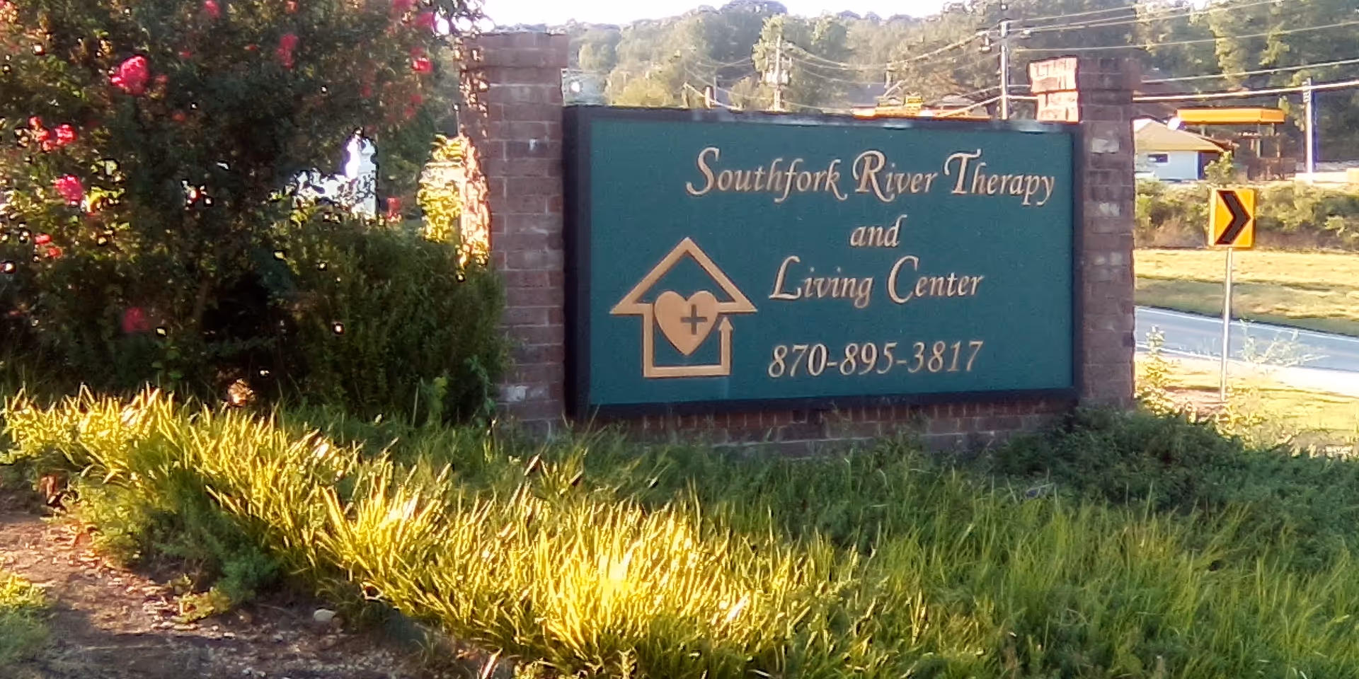 Outdoor teal sign for Southfork River Therapy and Living Center beside landscaped roadside plants