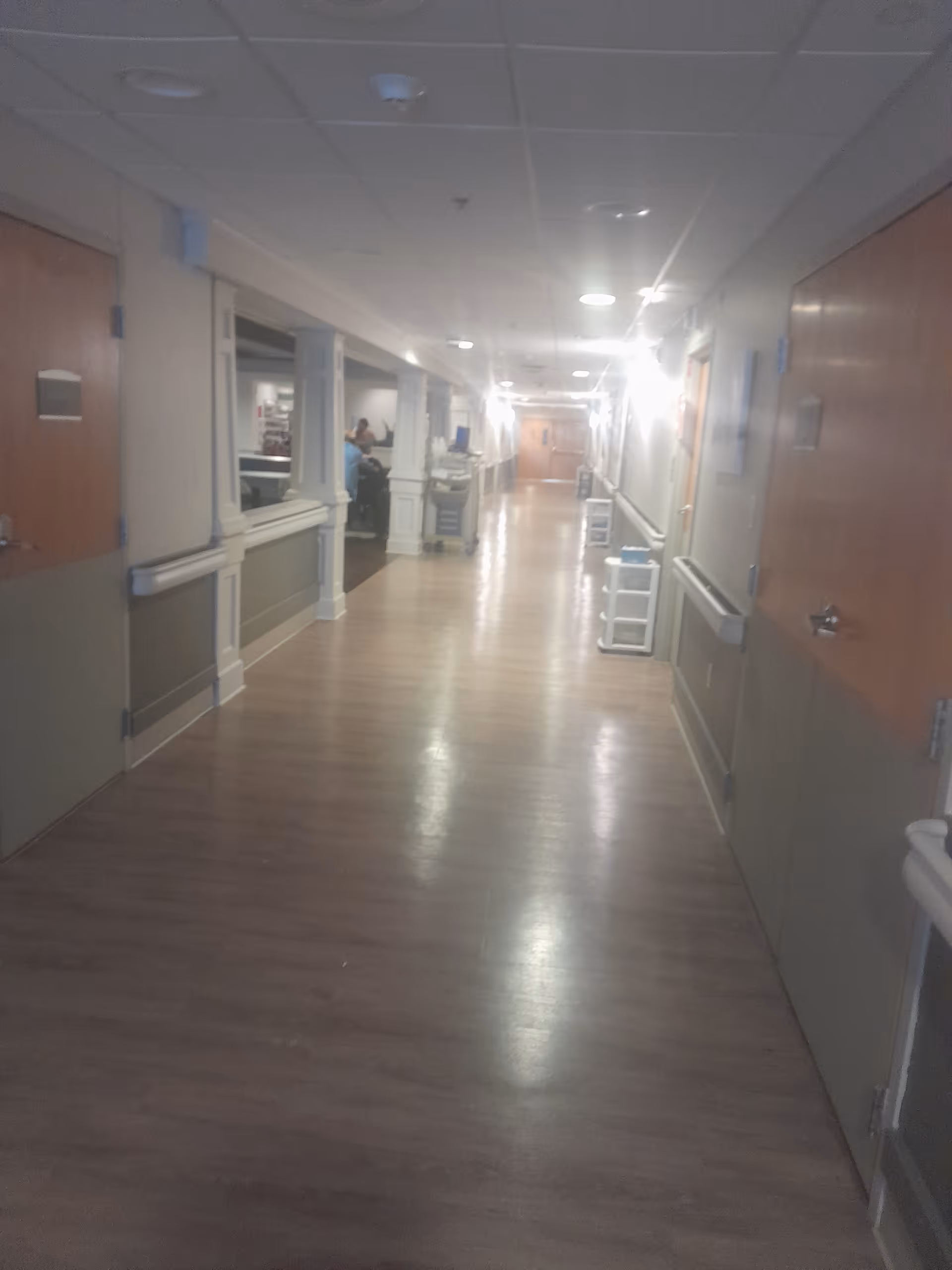 A long, well-lit nursing facility hallway with doors along both sides.