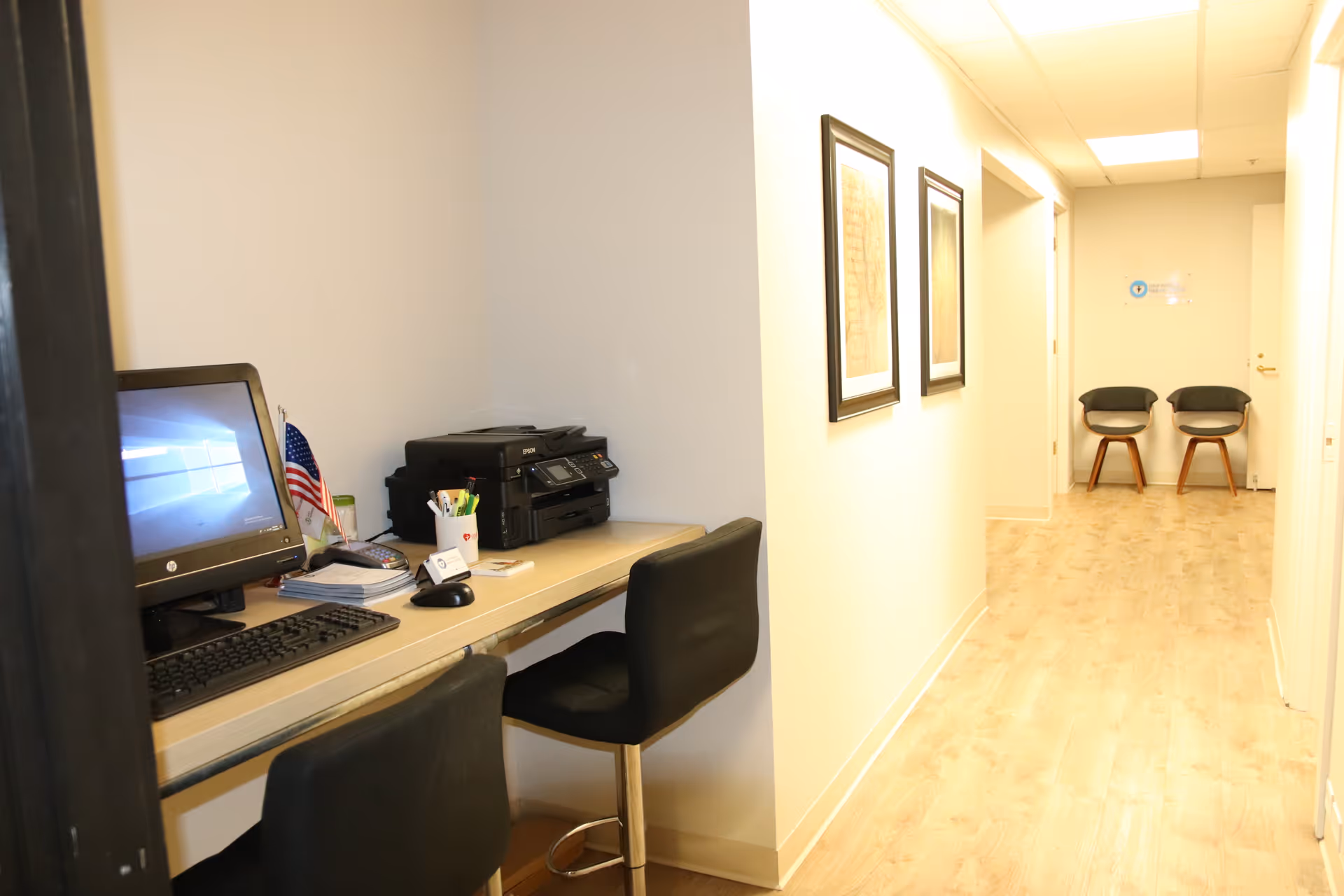 Hallway office area with a desk, computer, printer, and two waiting chairs.