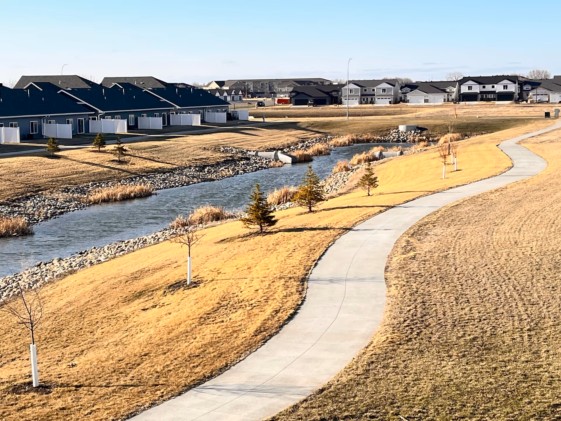 Expansive suburban complex with a winding path along a river and row of houses.