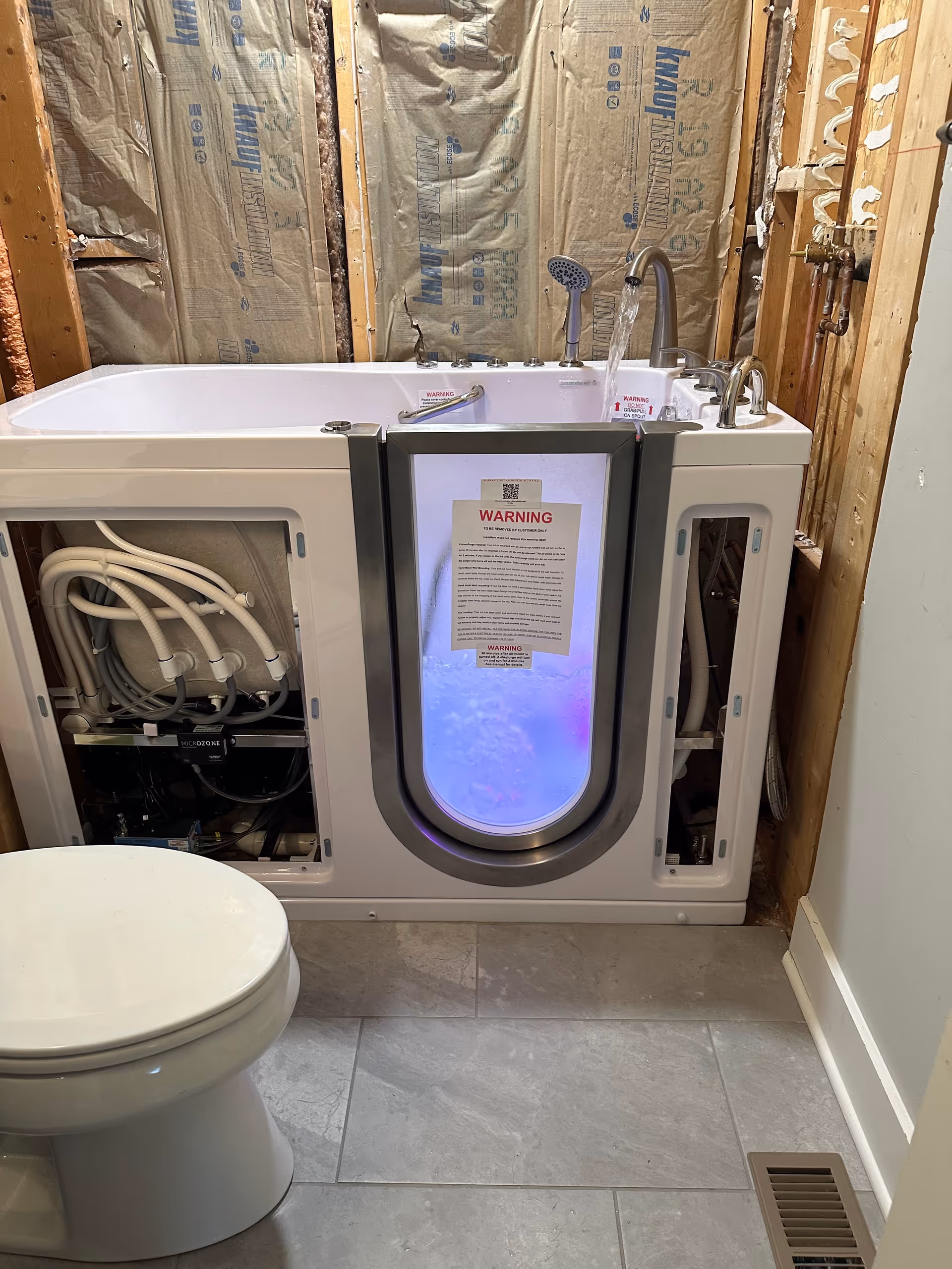 Under-construction accessible walk-in tub in bathroom with exposed insulation and toilet.