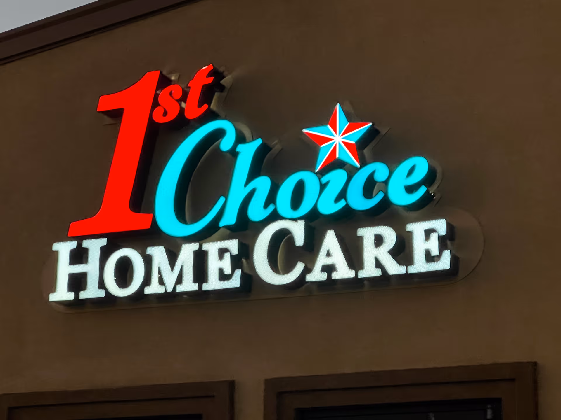 Bright neon sign reading 1st Choice Home Care mounted on a brown exterior wall.