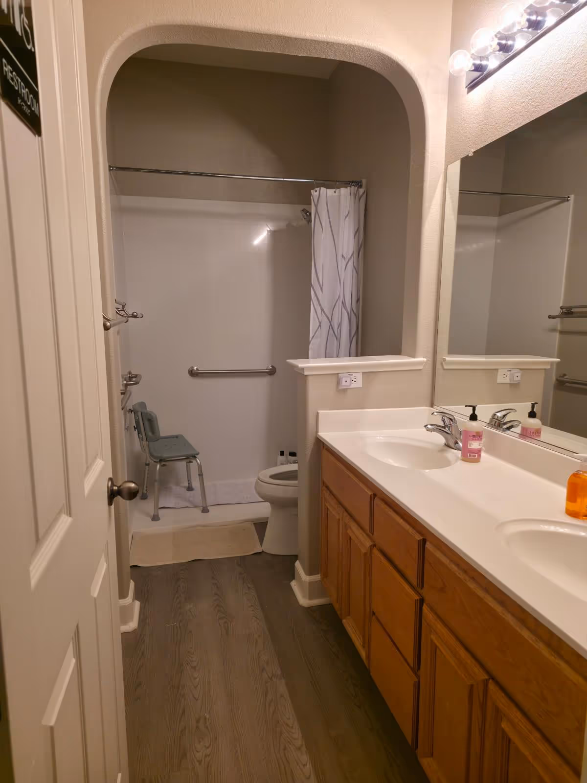 Accessible bathroom with sink, mirror, and a shower featuring a fold chair.