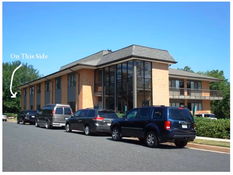 Two-story brick building with large glass windows and parked cars outside.