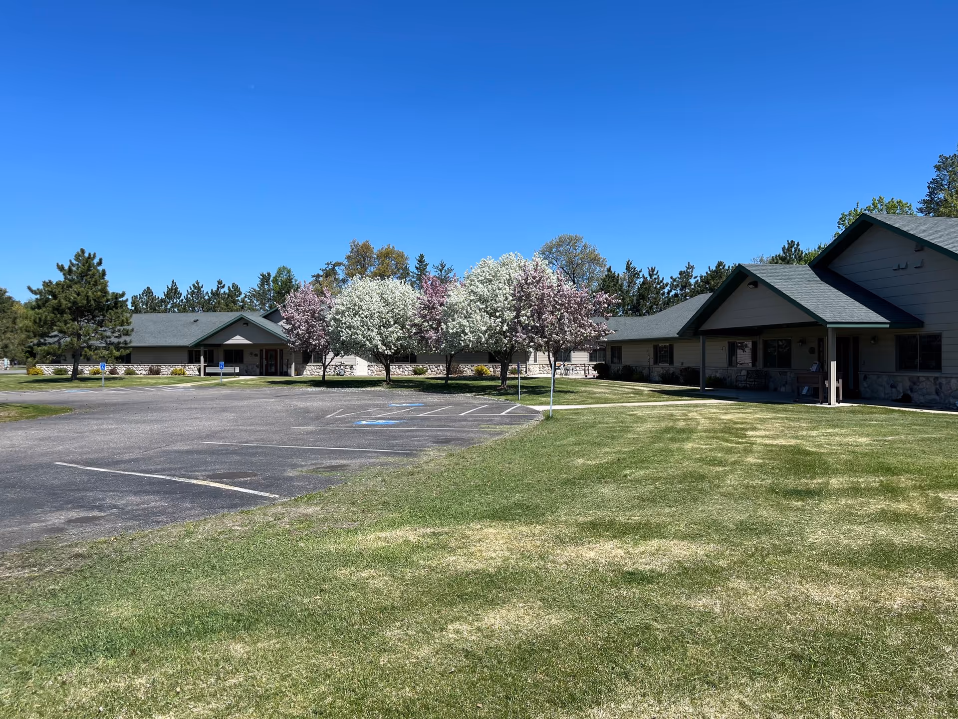 Exterior view of Nordic Woods Assisted Living facility with parking lot, lawn, and blooming trees.