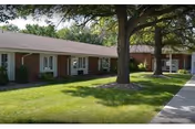 Single-story brick senior living facility with a green lawn and a large tree in front.