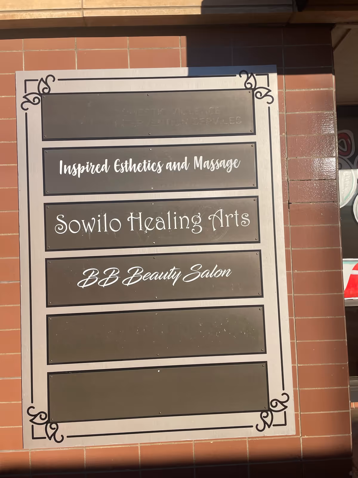 Framed exterior sign on brick wall listing Sowilo Healing Arts and related salons.