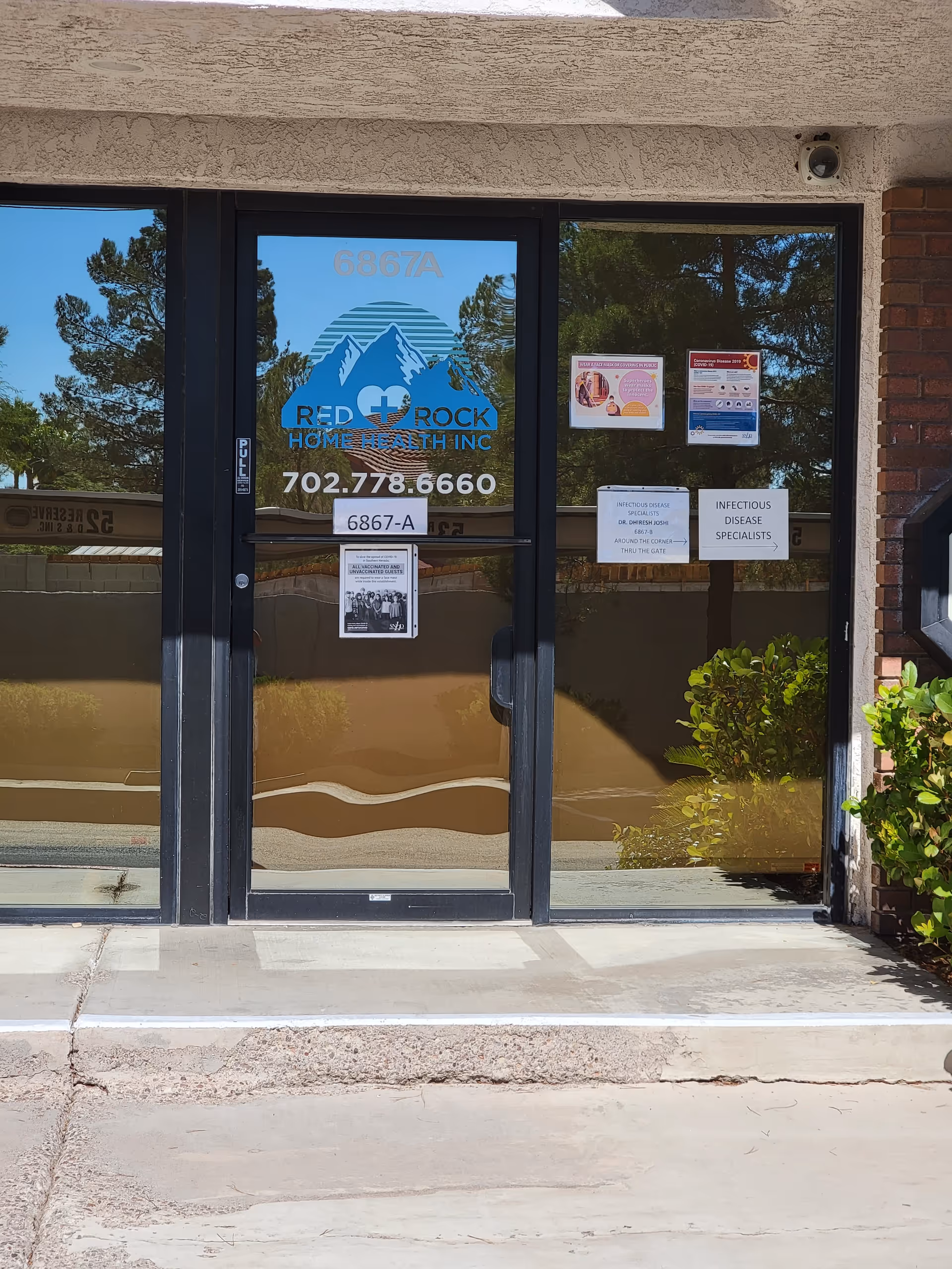 Glass entrance of Red Rock Home Health, Inc. with logo, posters, and plants outside.