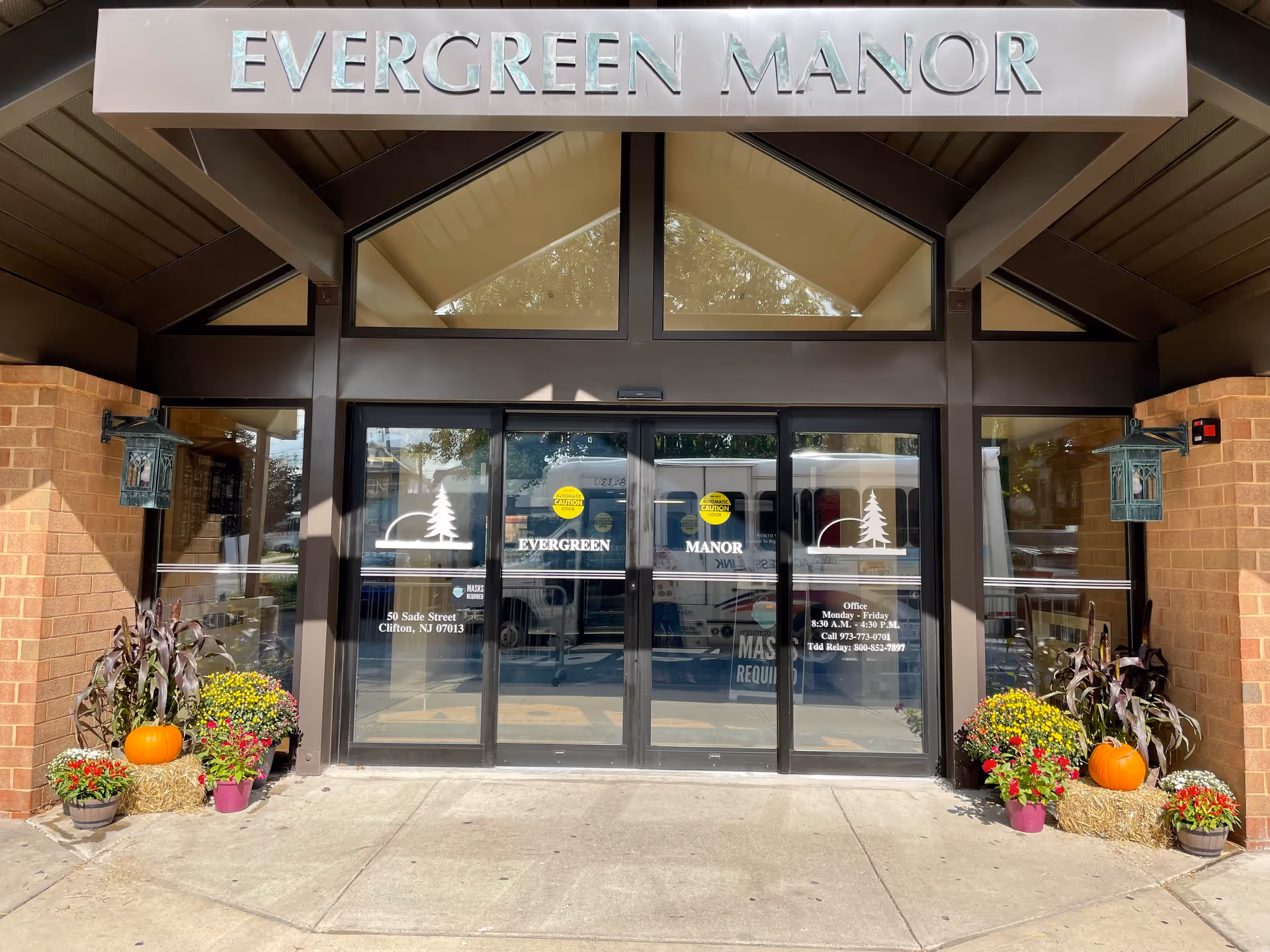 Entrance to Evergreen Manor senior living facility with glass doors and autumn plants.