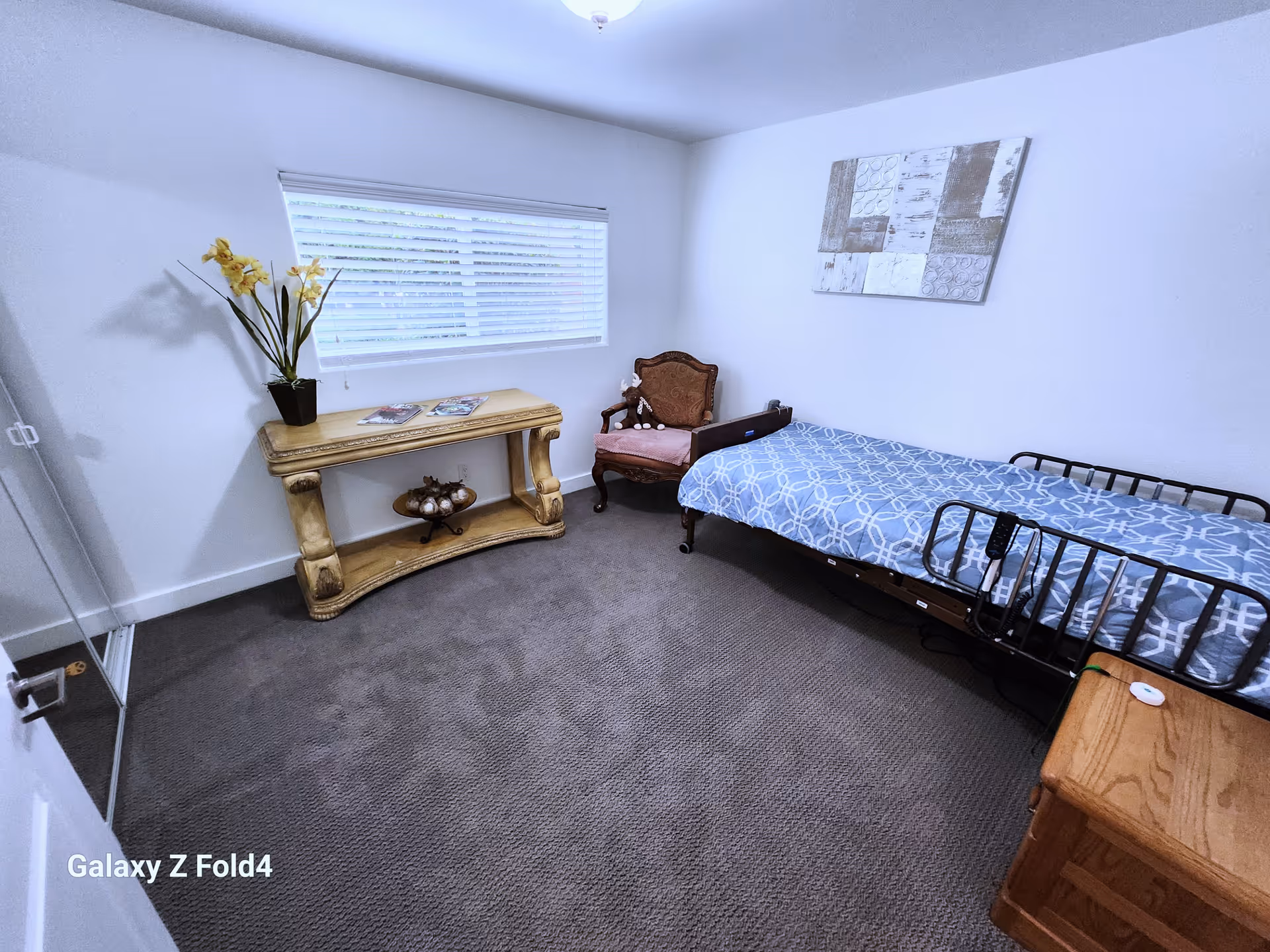 Small furnished bedroom with a single bed, chair, console table, window, and wall art.