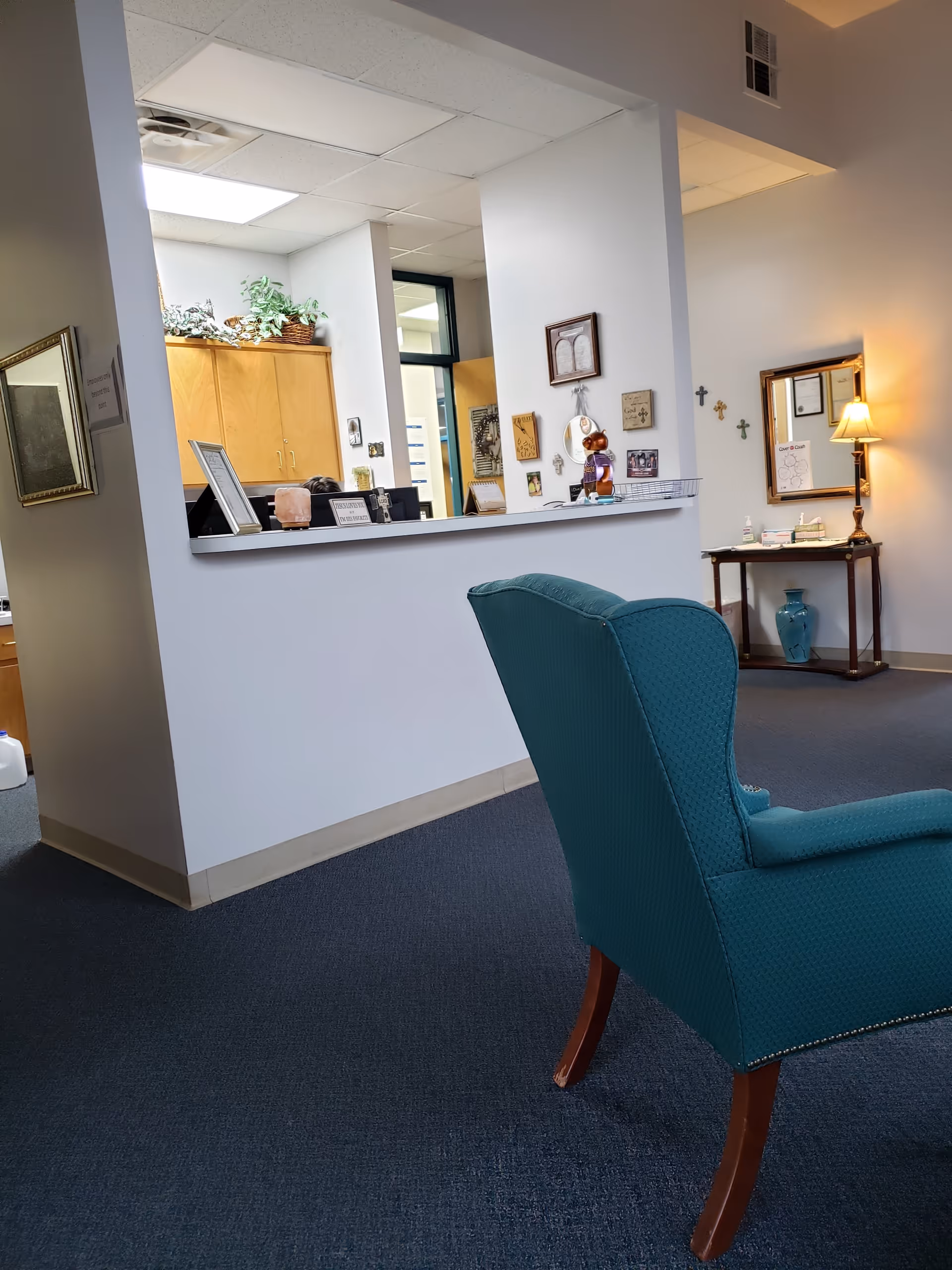 Teal upholstered chair in a quiet reception area with a service counter and wall decor.
