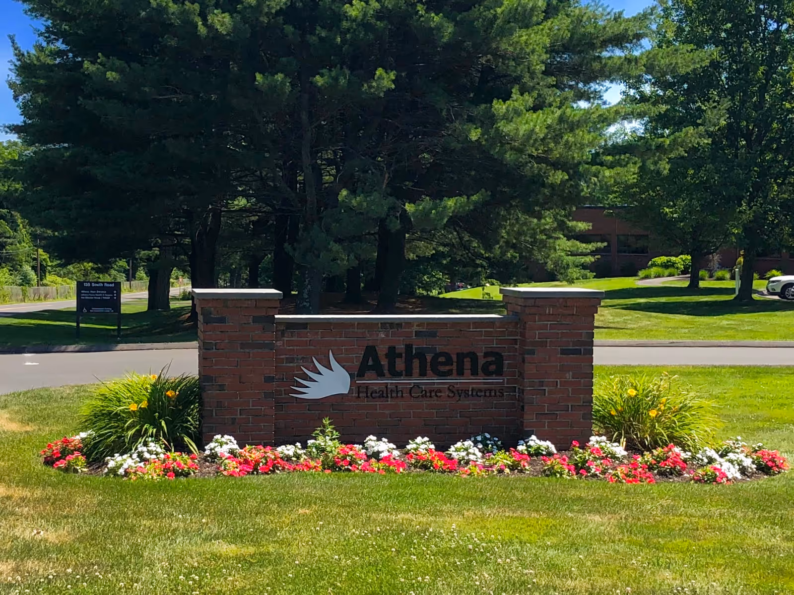 Outdoor brick sign for Athena Health Care Systems surrounded by flowers and trees.
