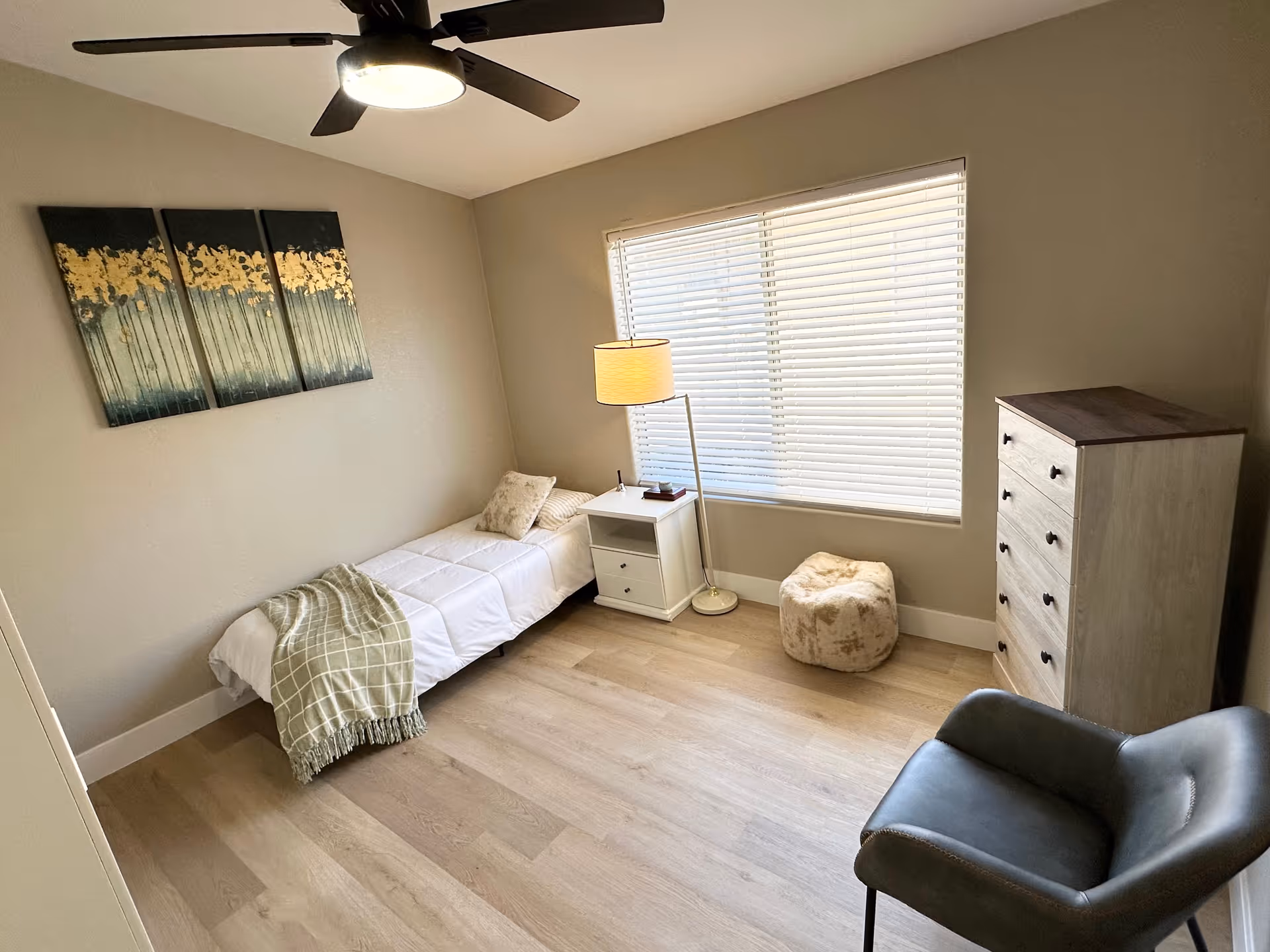 Small bedroom with a single bed, dresser, window blinds, lamp, and ceiling fan.