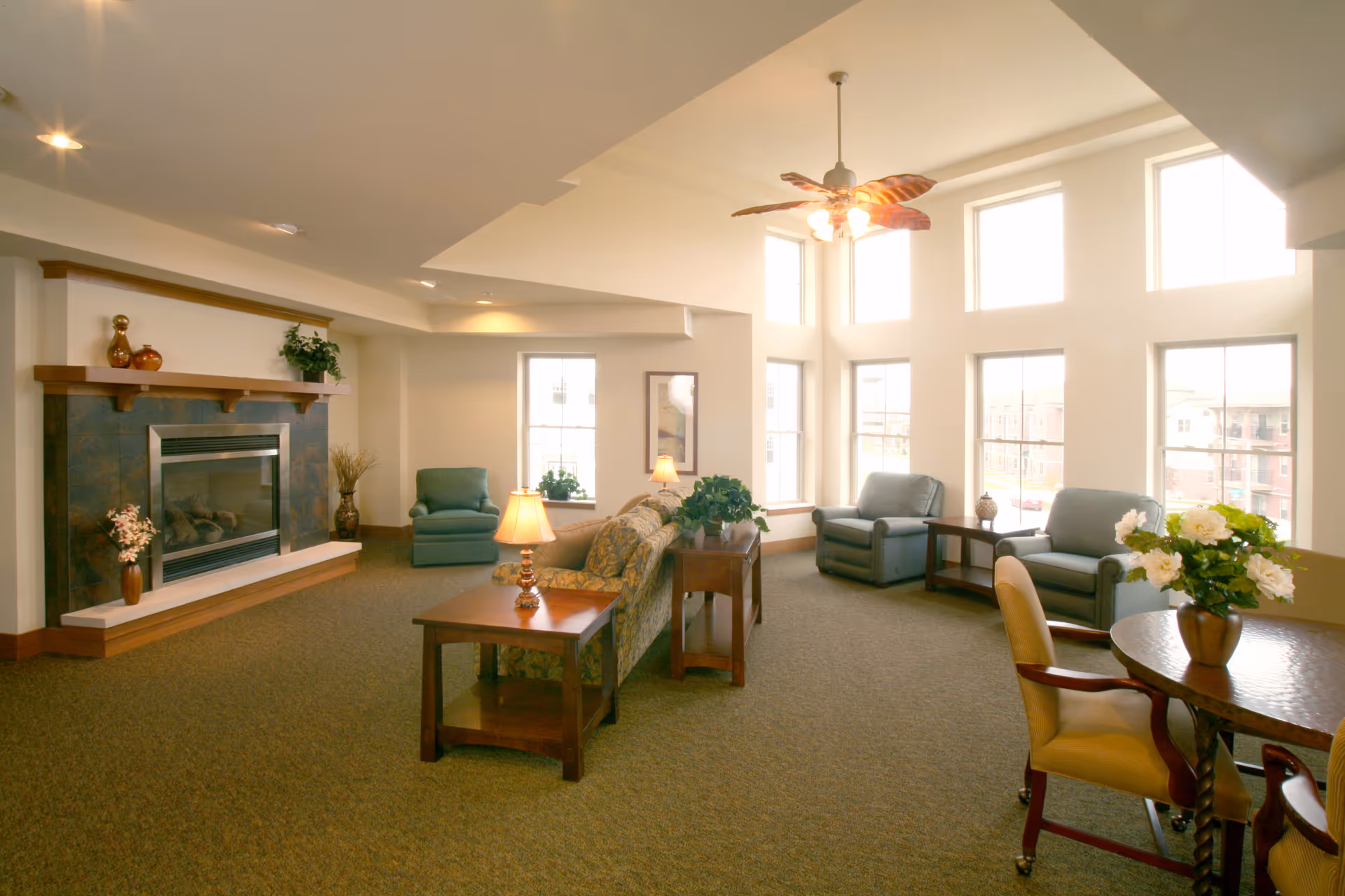Bright senior living lounge with fireplace, seating, and large windows in a communal living area.