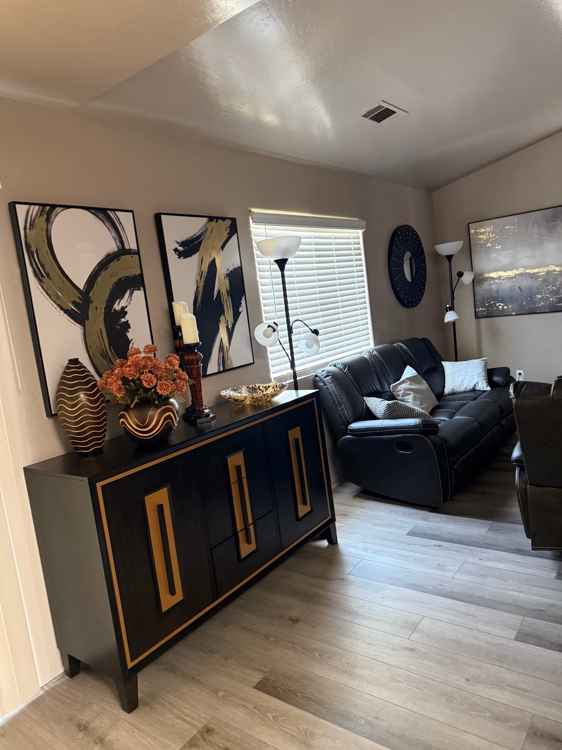 A modern living room with a black leather sofa, console cabinet, and abstract art.