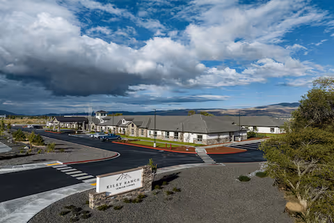 A modern senior living campus with light-colored buildings, roads, and a sign.