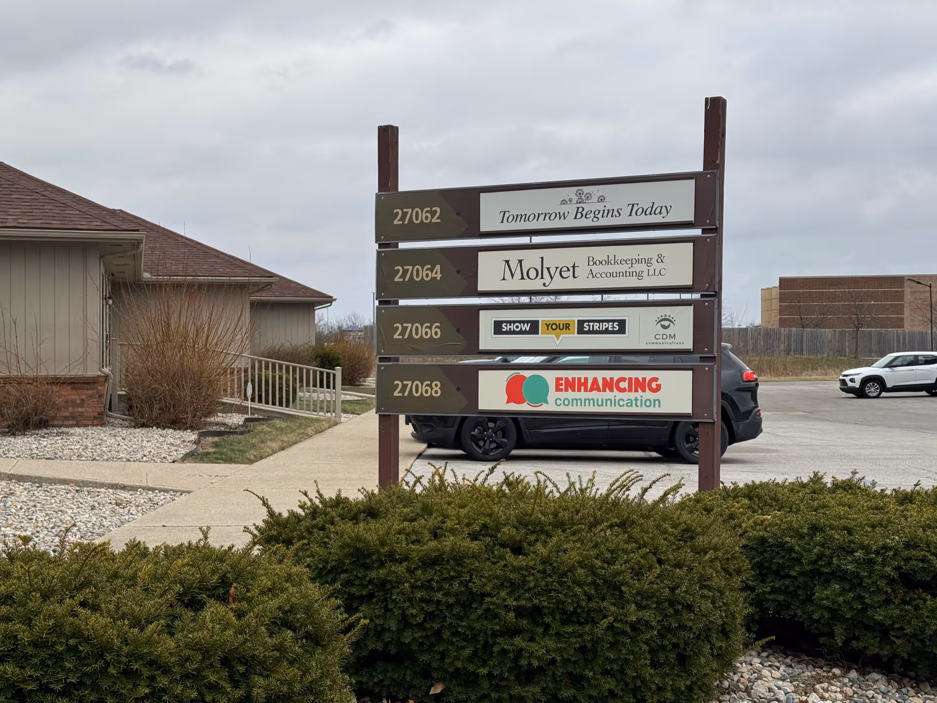 Outdoor signpost with multiple business names in front of a building.