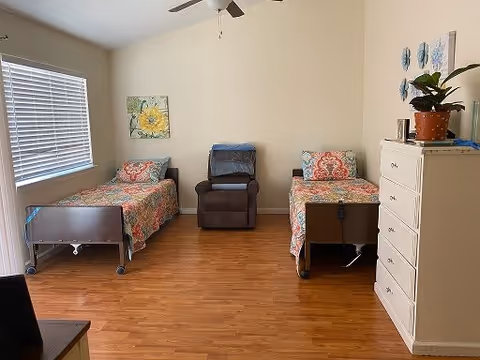 A bright shared bedroom with two twin beds, a recliner between them, a dresser, and a window with blinds.