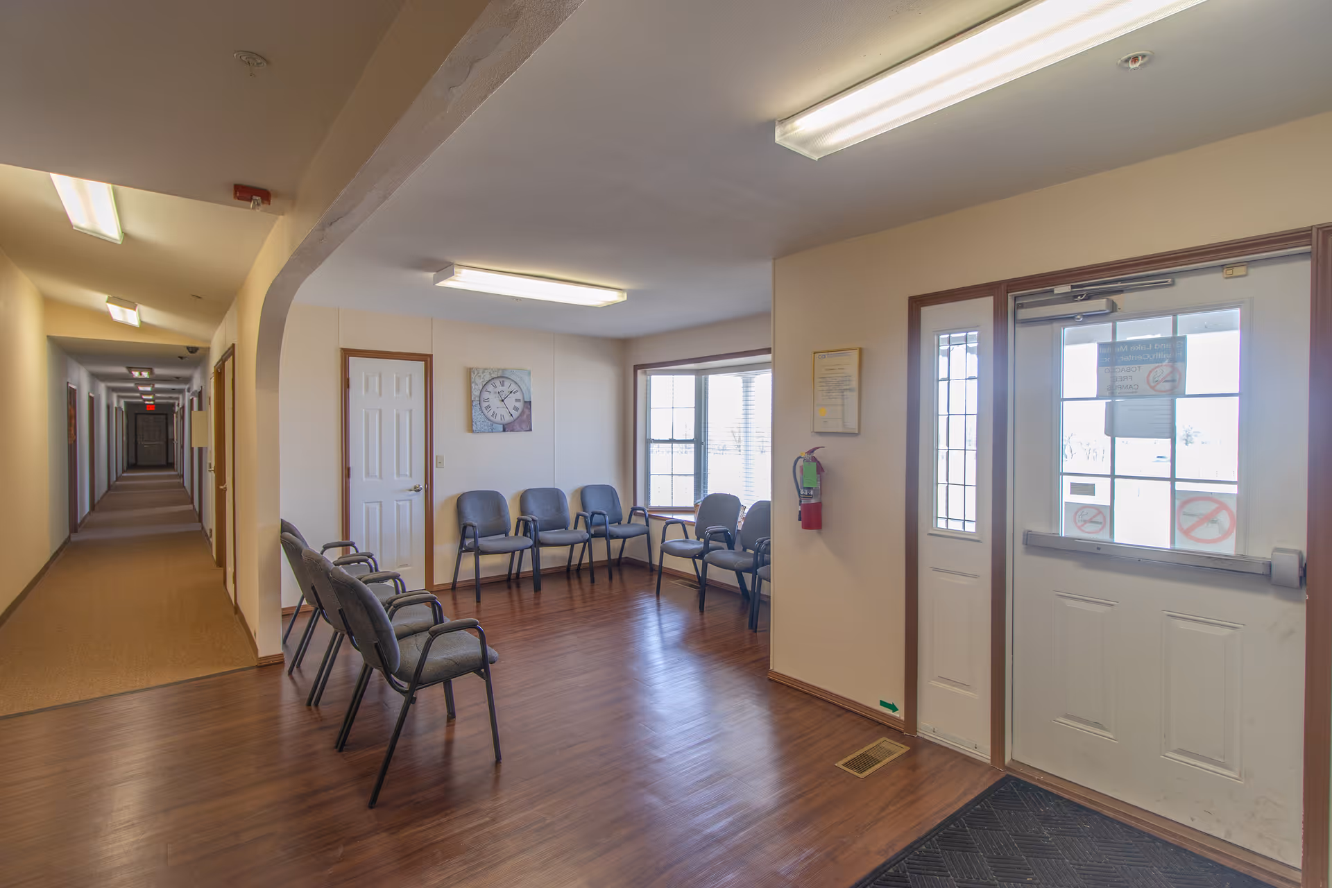 Interior hallway and waiting area with chairs along the wall and glass-front door.