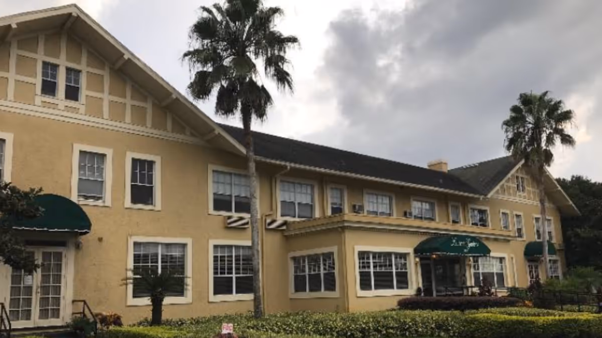 Exterior view of a yellow senior living building with green awnings and palm trees.