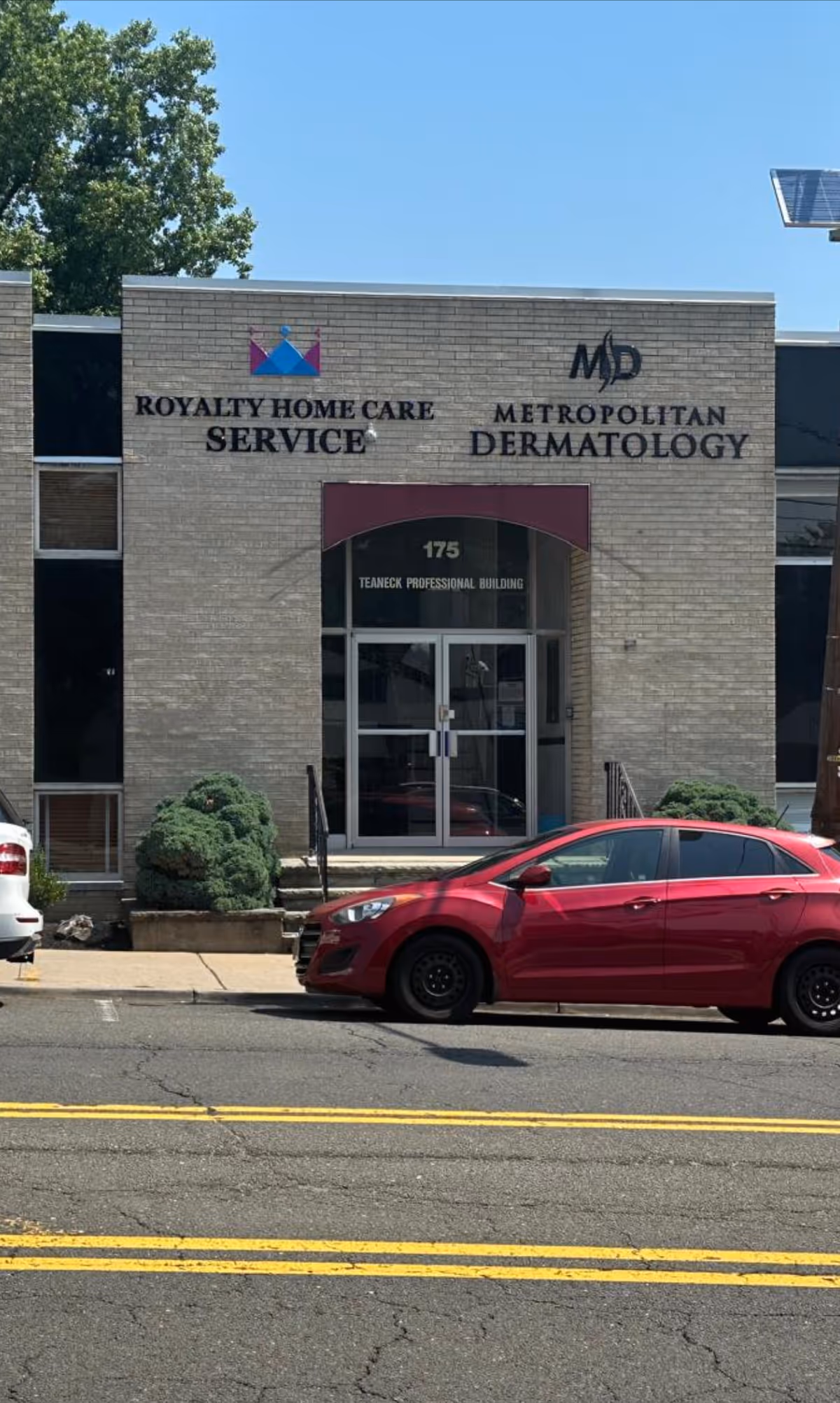 Brick building storefront with Royalty Home Care Service and Metropolitan Dermatology signs, and a red car.