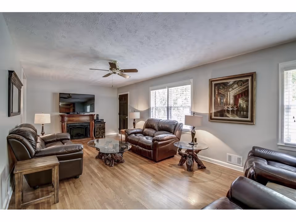 Cozy living room with leather seating, glass coffee tables, a fireplace, and a ceiling fan.