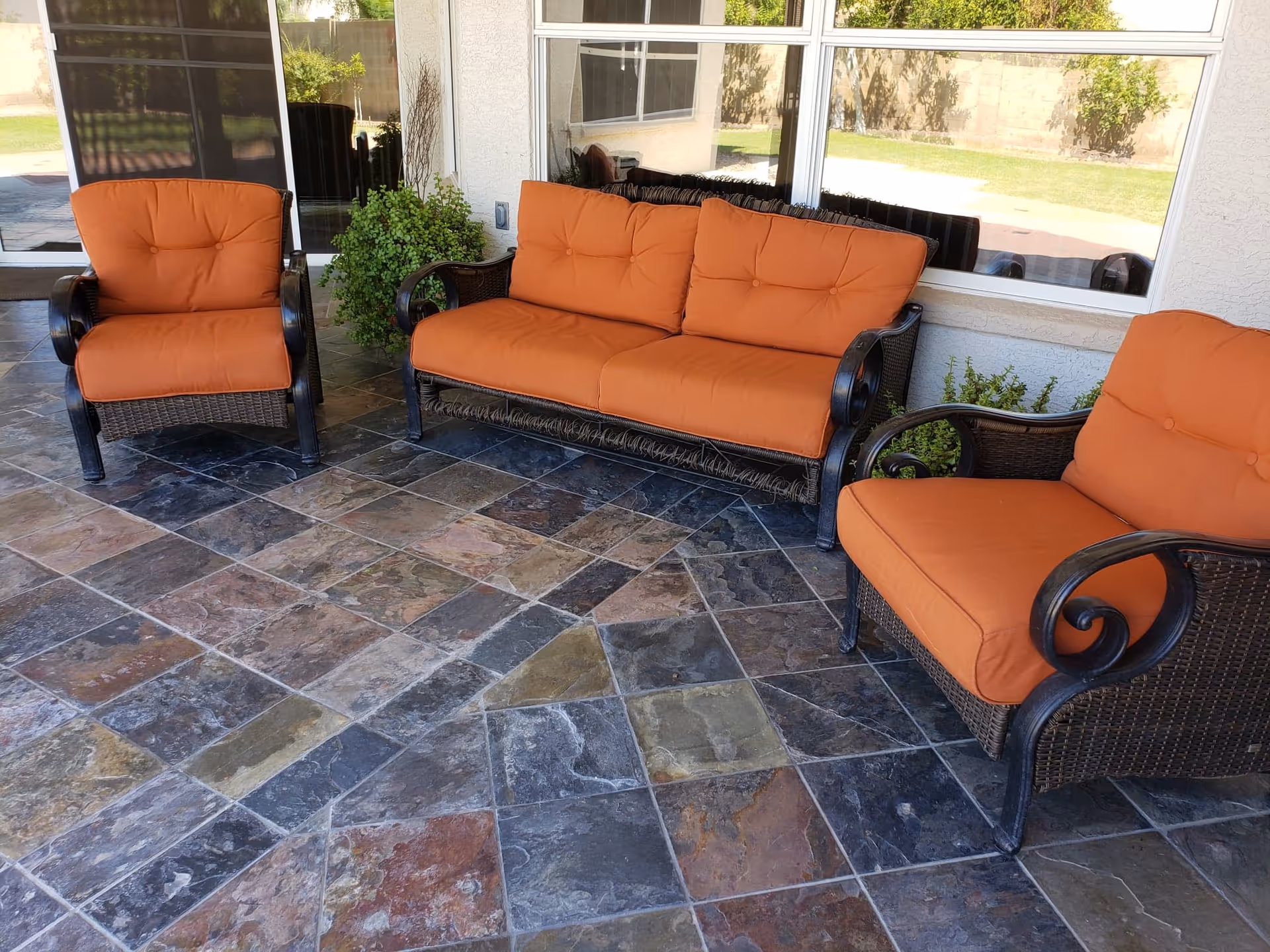 Patio seating with orange cushions on wicker furniture along a tiled outdoor porch.