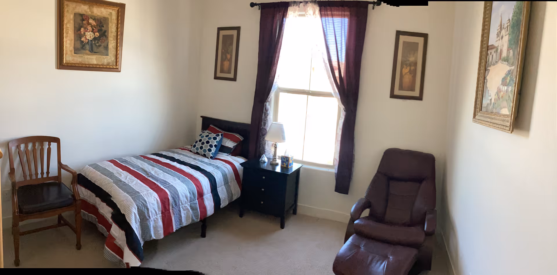 Cozy bedroom with single bed, nightstand, lamp, window with purple curtains, and a recliner.