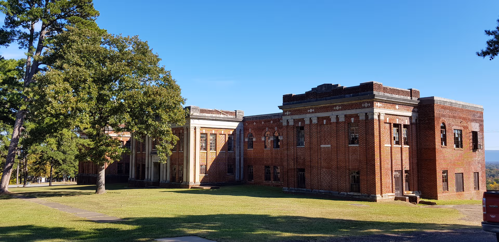 Brick building exterior with a lawn, trees, and blue sky.